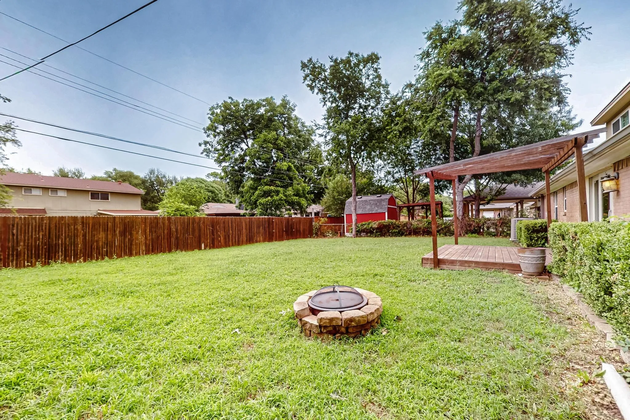 Fenced backyard with a fire pit, a wooden deck, and a storage unit