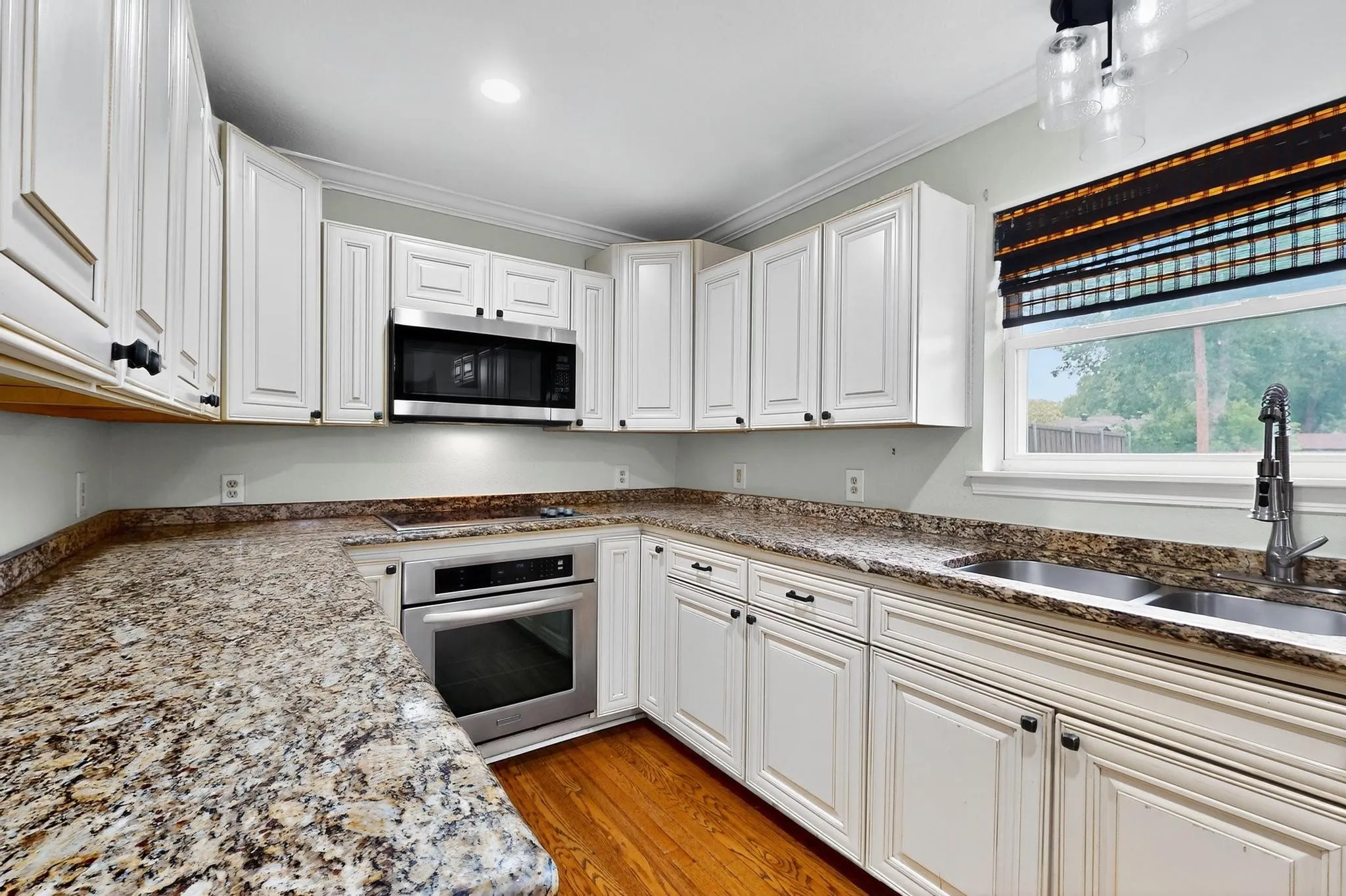 Kitchen with appliances with stainless steel finishes, ornamental molding, white cabinetry, light wood-type flooring, and stone counters