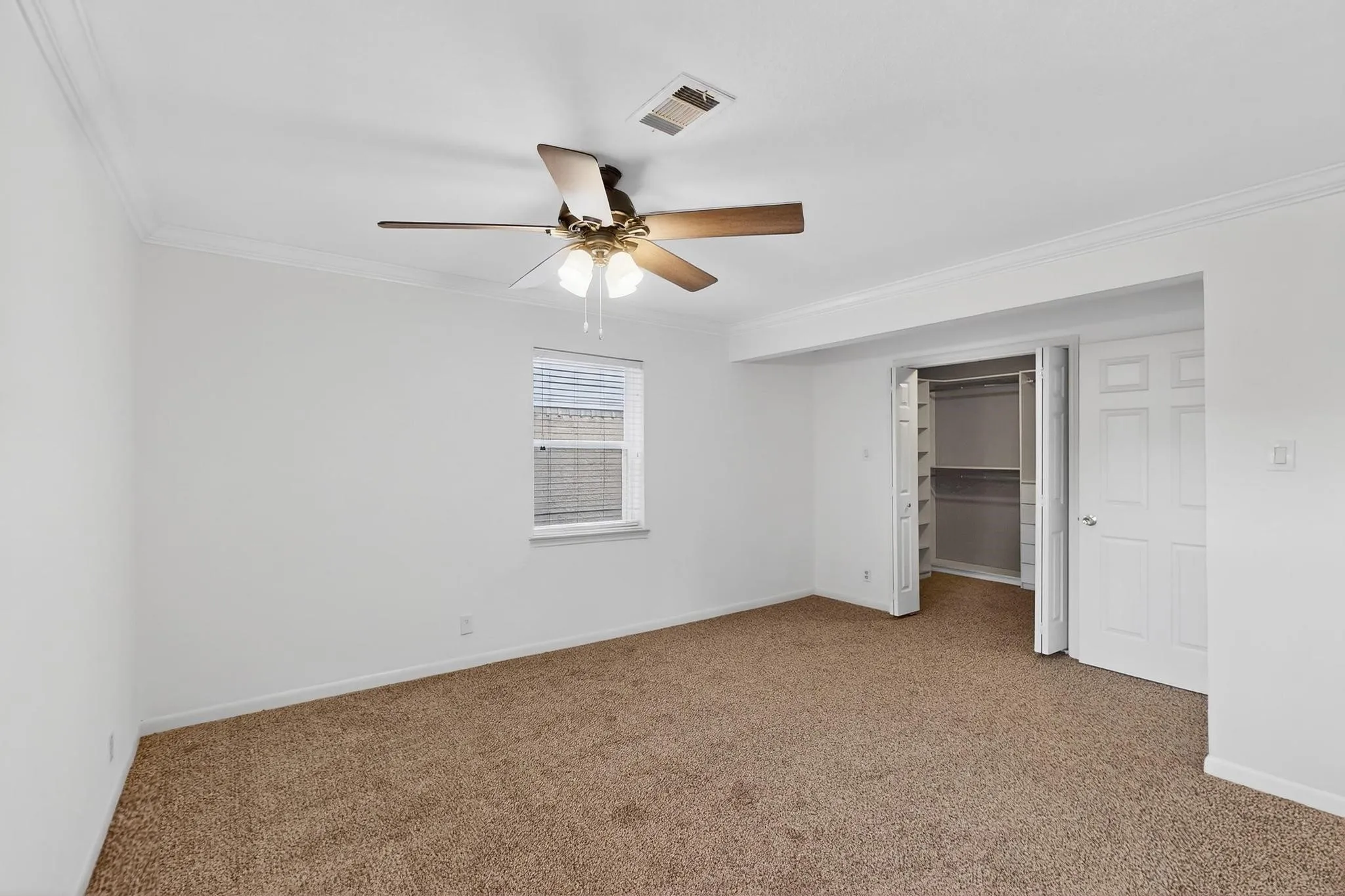 Unfurnished bedroom featuring ornamental molding, carpet flooring, ceiling fan, a walk in closet, and a closet