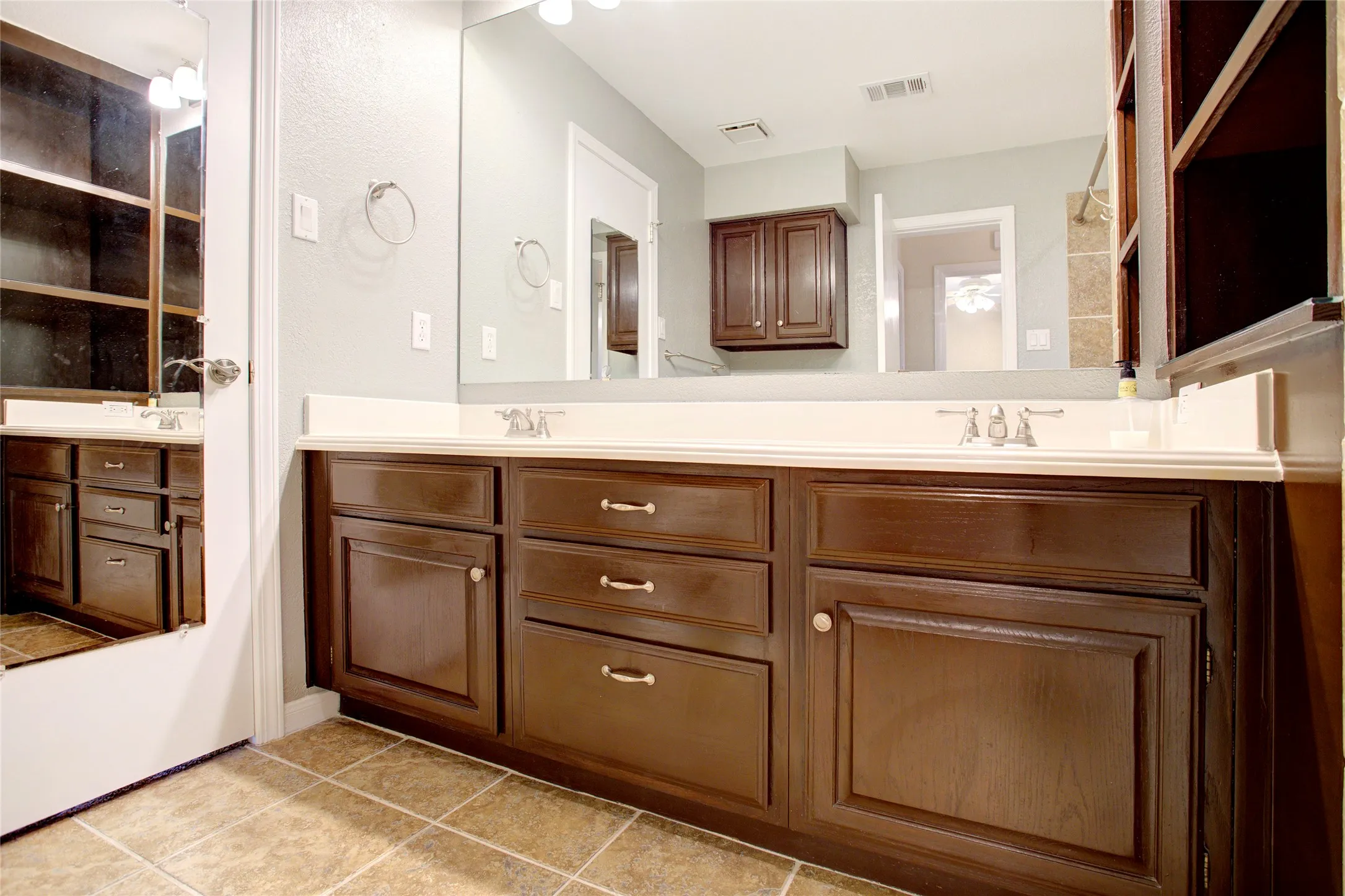 Double vanity with dark wood-finish cabinetry, integrated sinks, large mirror, and tile flooring