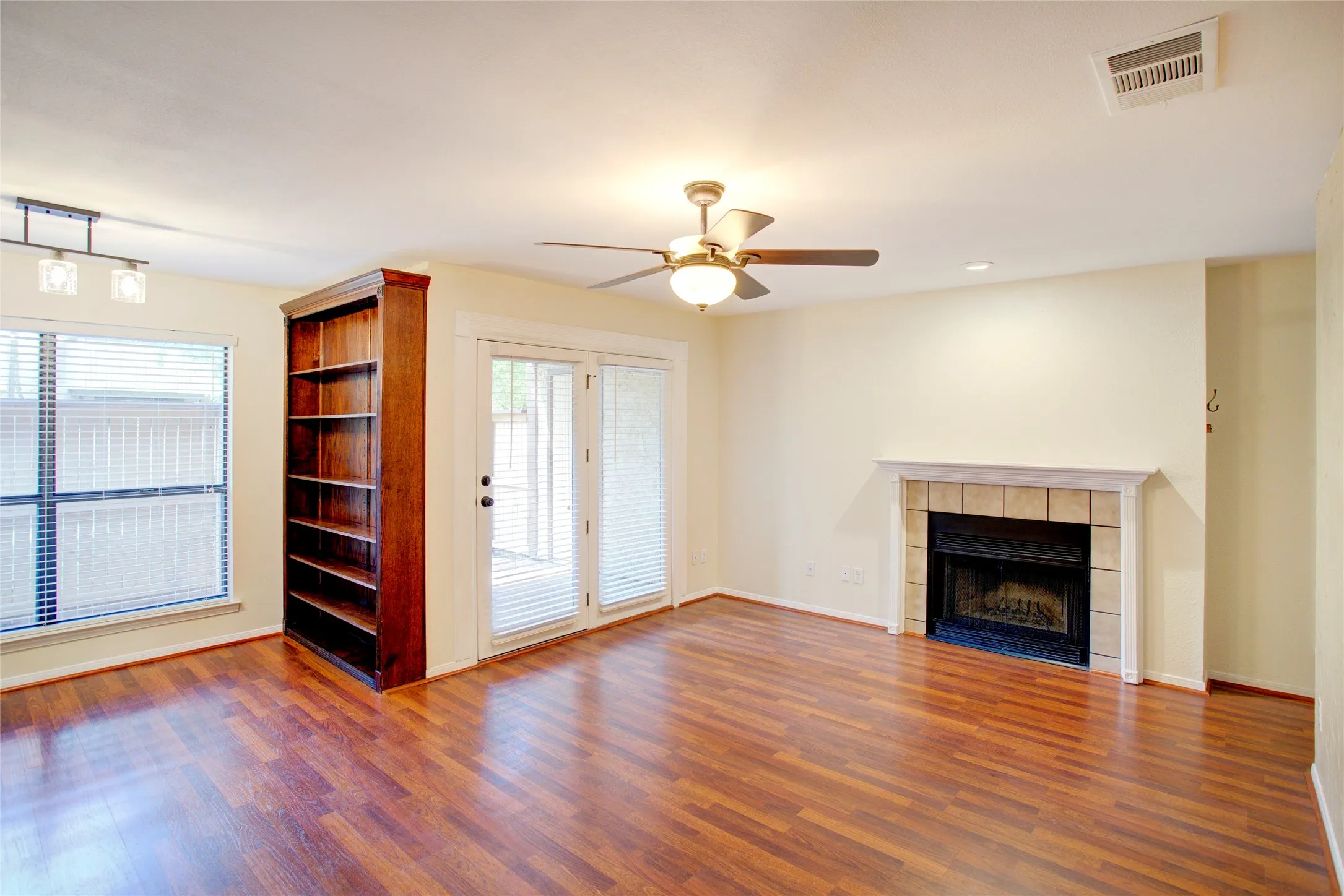 Wood-finish flooring, built-in shelving, tile-surround fireplace with mantel, ceiling fan, and double-pane glass doors