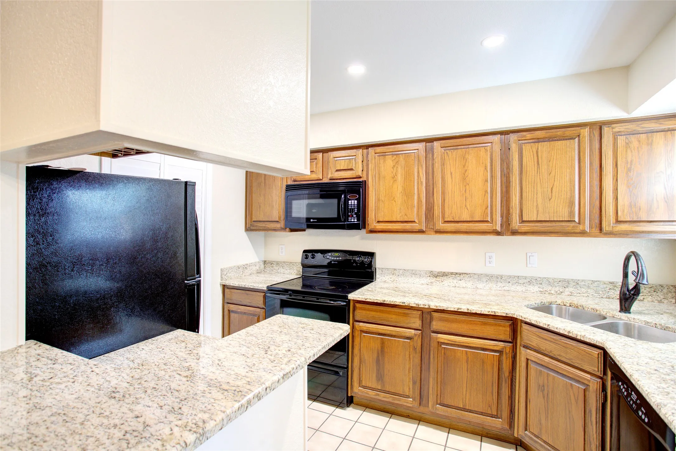 Kitchen featuring wood cabinetry, granite countertops, black appliances, a double basin sink, and recessed lighting