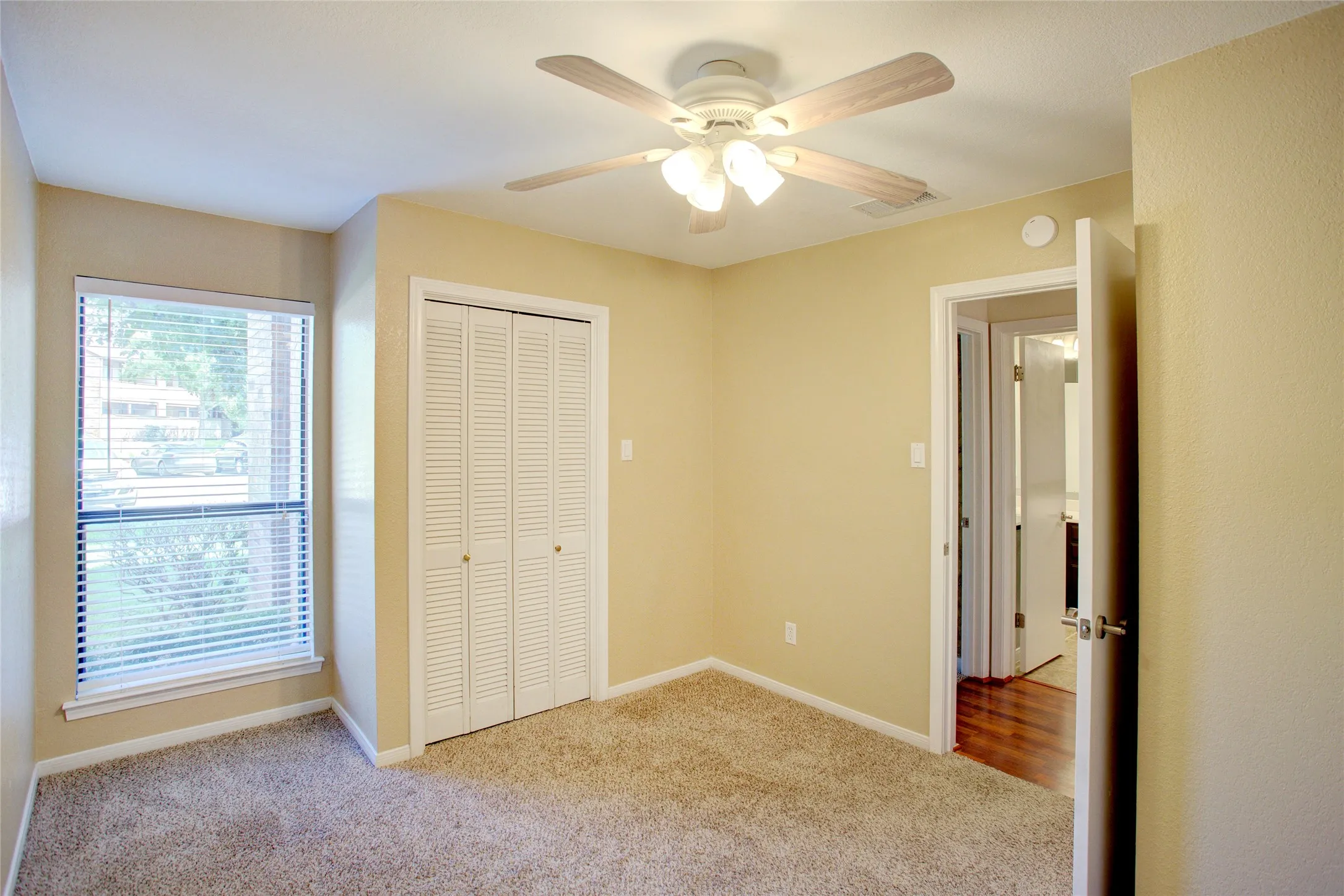Carpeted room featuring a window with blinds, bi-fold louvered closet doors, and a ceiling fan with light fixture