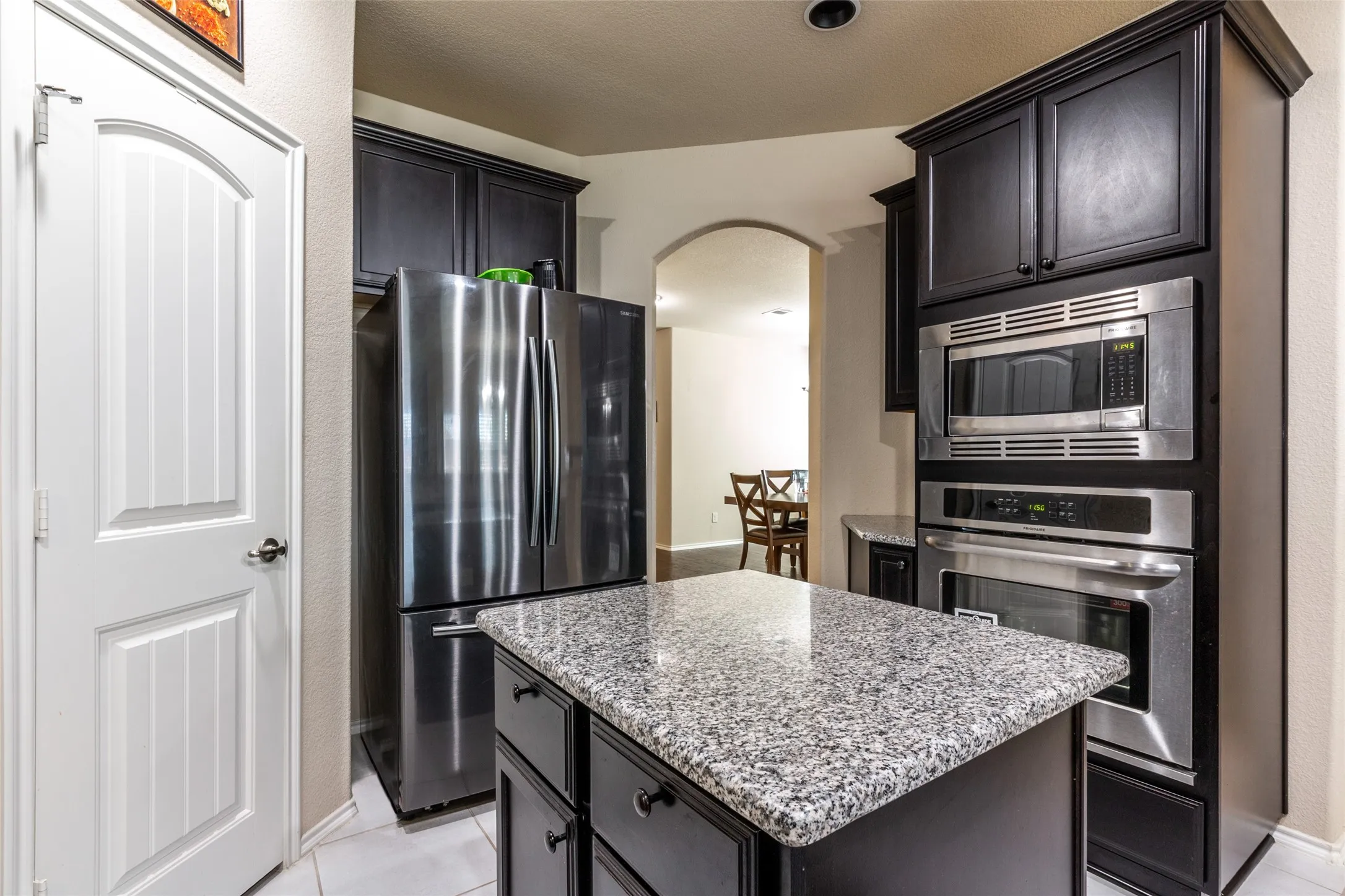 Kitchen with appliances with stainless steel finishes, arched walkways, a kitchen island, light stone counters, and light tile patterned flooring