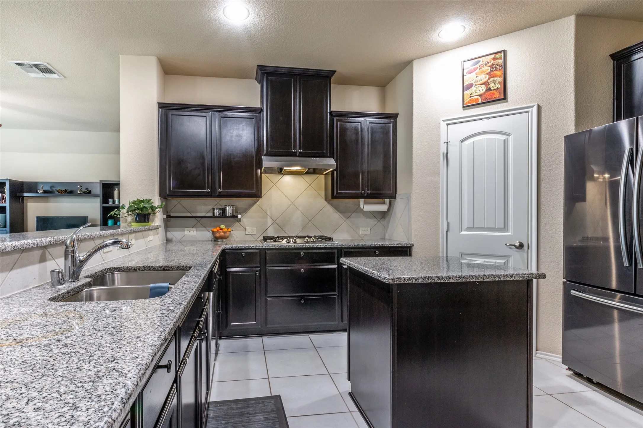 Kitchen featuring appliances with stainless steel finishes, under cabinet range hood, light stone counters, backsplash, and light tile patterned floors