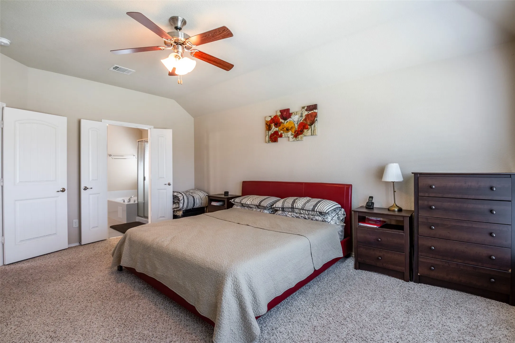 Carpeted bedroom with vaulted ceiling, ceiling fan, and ensuite bathroom