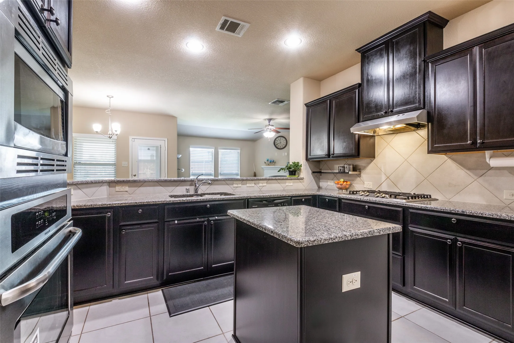 Kitchen featuring stainless steel appliances, under cabinet range hood, decorative backsplash, light stone counters, and recessed lighting