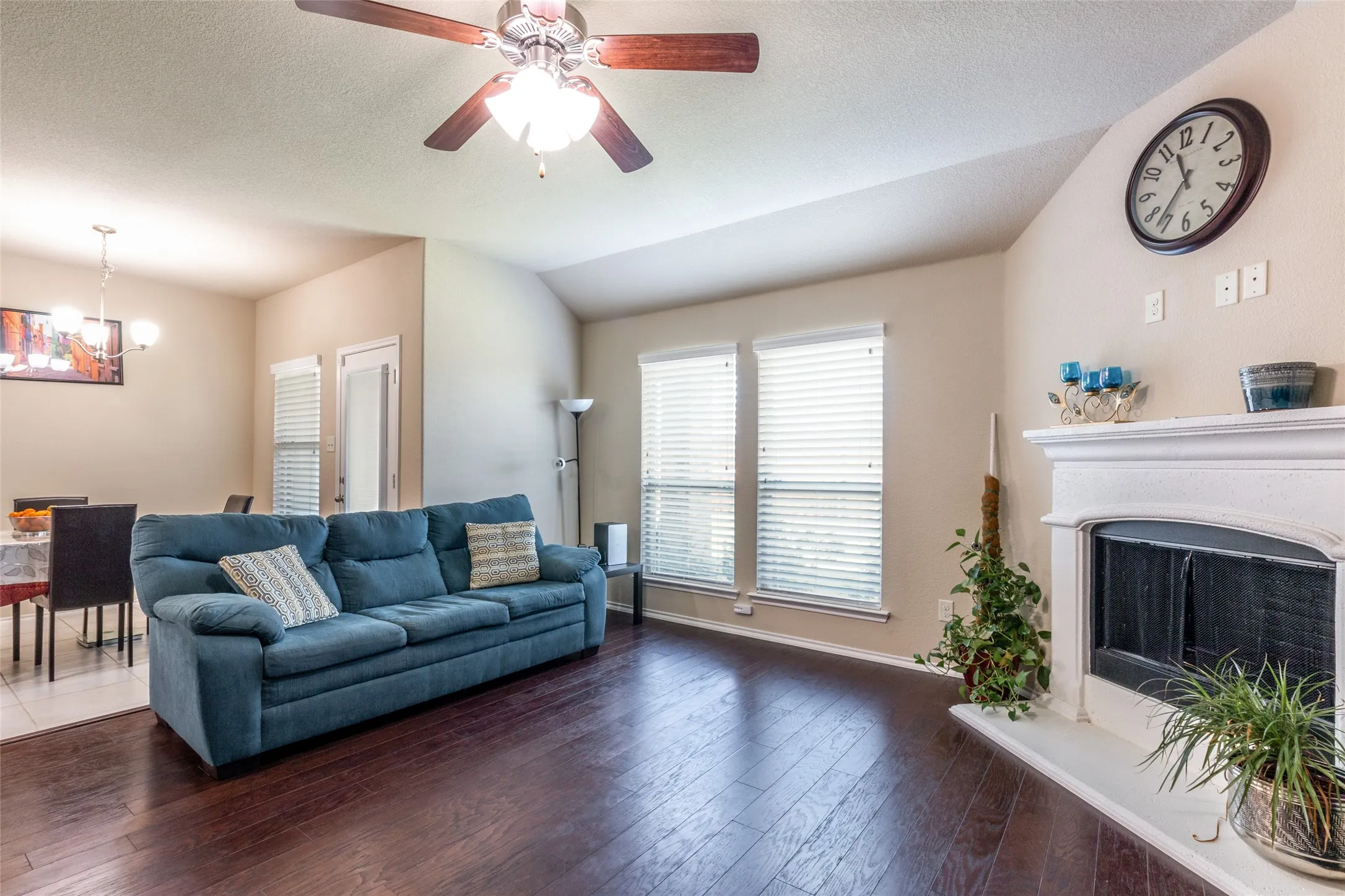 Living area featuring a chandelier, dark wood-type flooring, ceiling fan, vaulted ceiling, and a fireplace with raised hearth