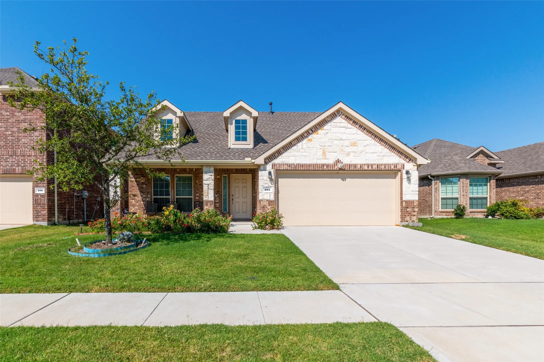 View of front of home with a front yard, a garage, brick siding, and driveway