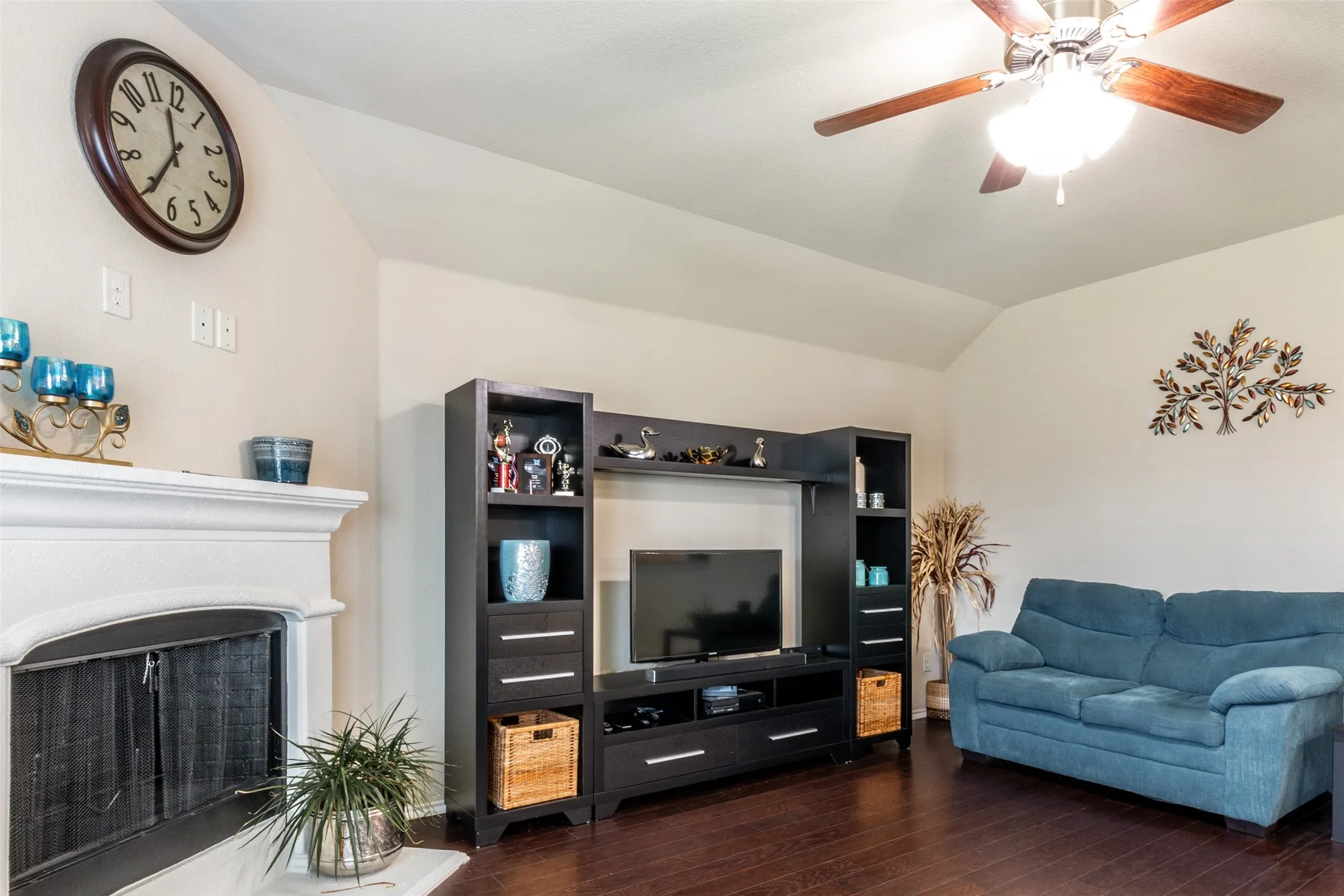 Living room featuring hardwood / wood-style flooring, lofted ceiling, ceiling fan, and a fireplace with raised hearth