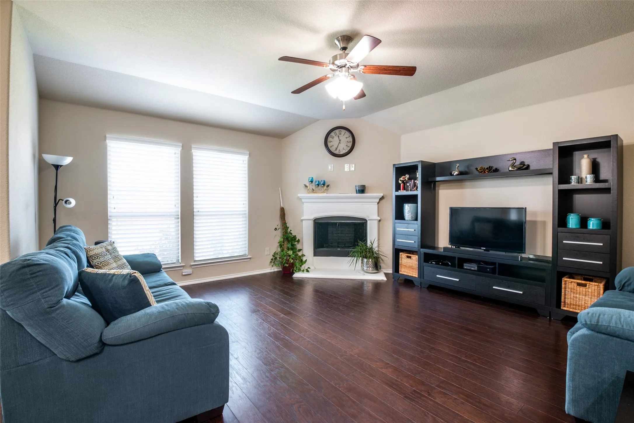 Living area featuring ceiling fan, dark wood-type flooring, vaulted ceiling, and a fireplace with raised hearth