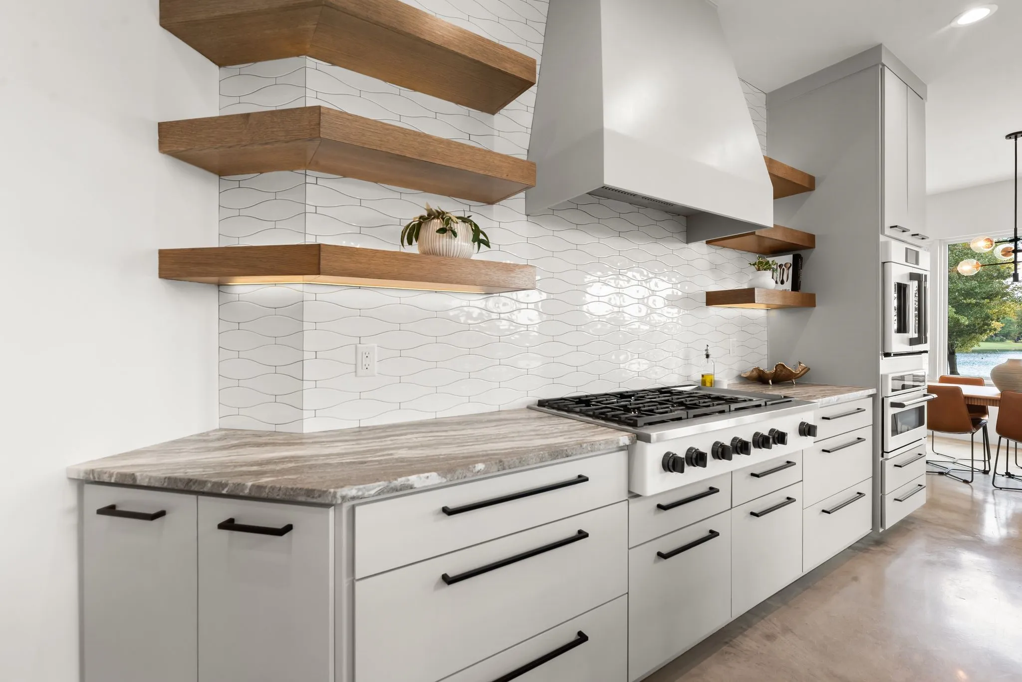 Custom kitchen details include open floating shelves, generous cabinetry, stone countertops, and convenient workspace in this Corsicana lake home.