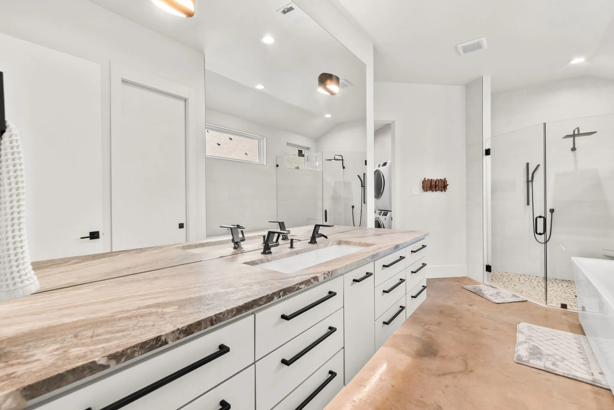 Luxury primary bathroom features an expansive double vanity, abundant cabinetry, stone countertops, and modern fixtures.