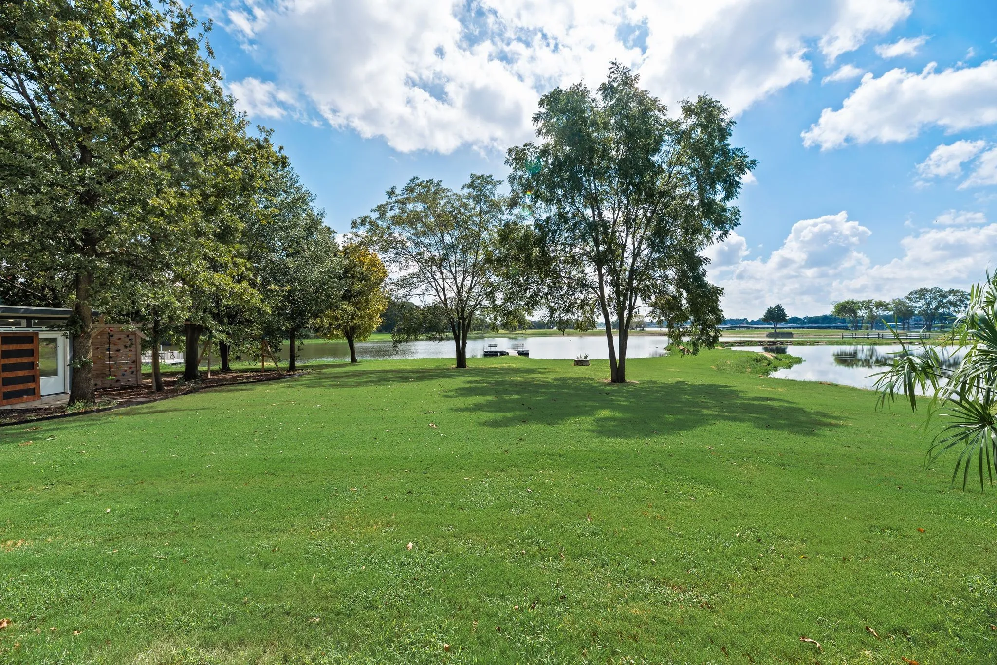 View from the covered back porch showcases the expansive grassy backyard, mature trees, and peaceful waterfront setting.