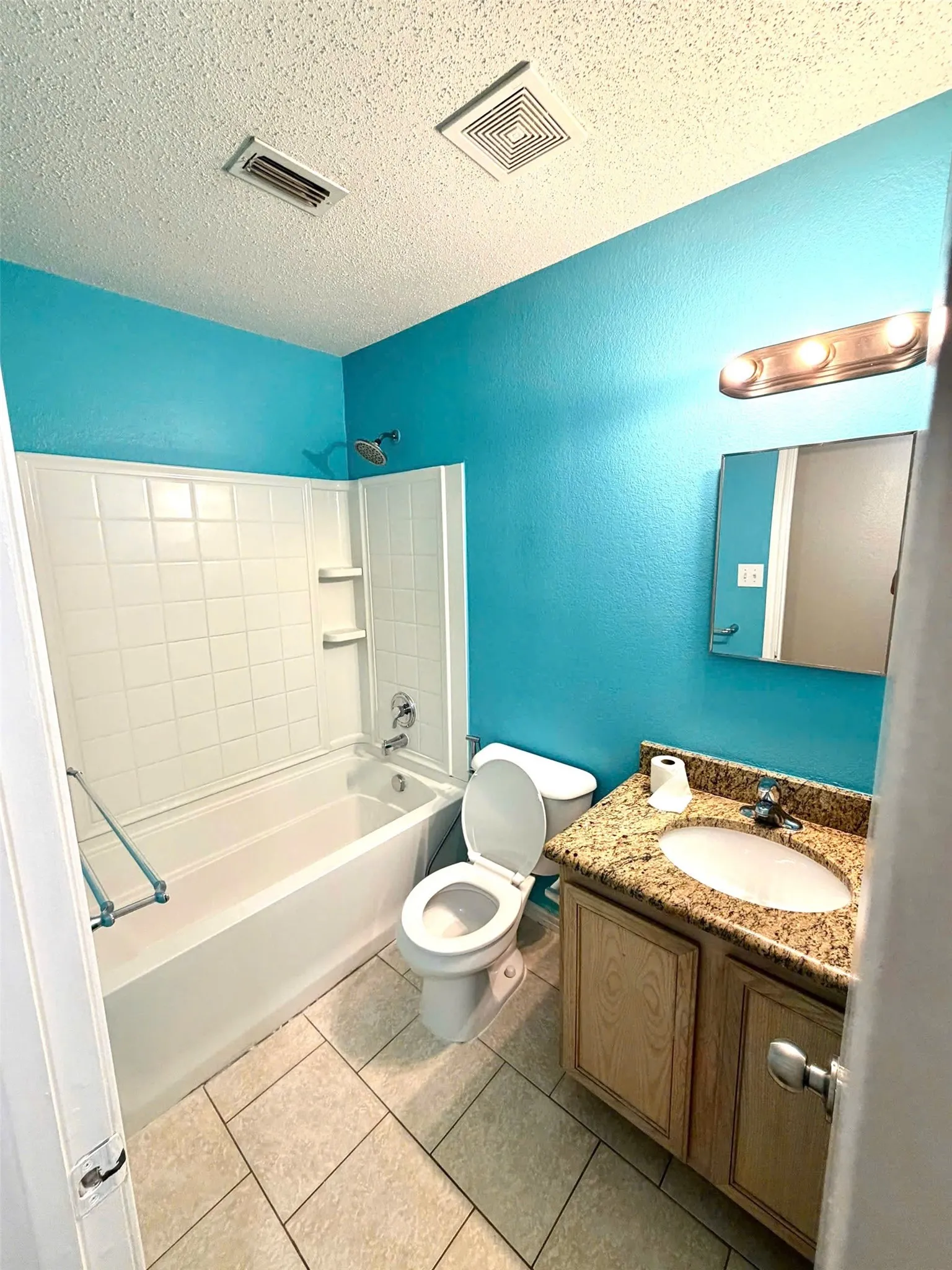 Bathroom featuring a tub/shower combination with white tile surround, a single vanity with stone-finish countertop, and tile flooring