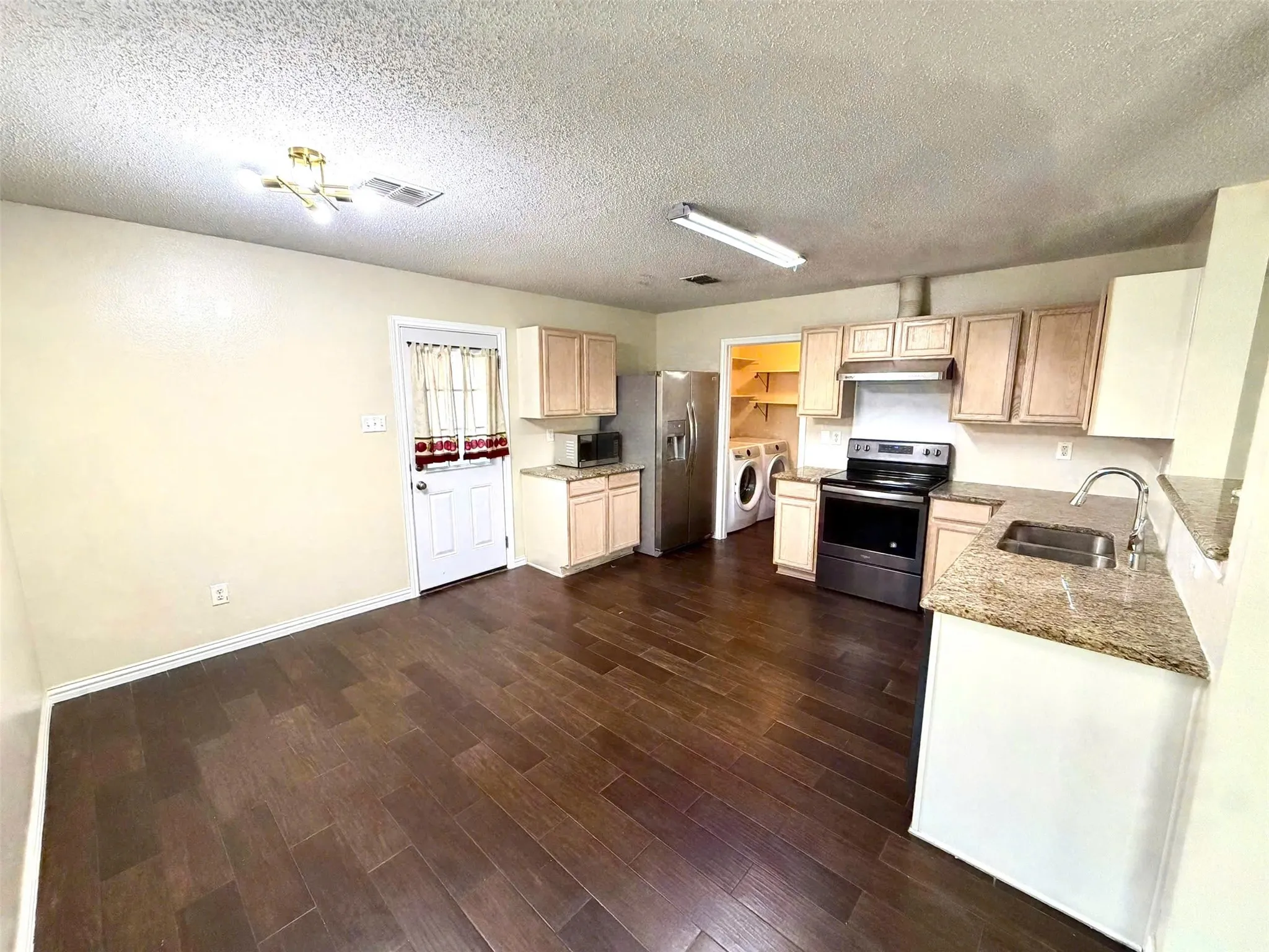 Wood-finish flooring, light-toned cabinetry, granite countertops, stainless steel sink with a gooseneck faucet, and a dedicated laundry area with shelving