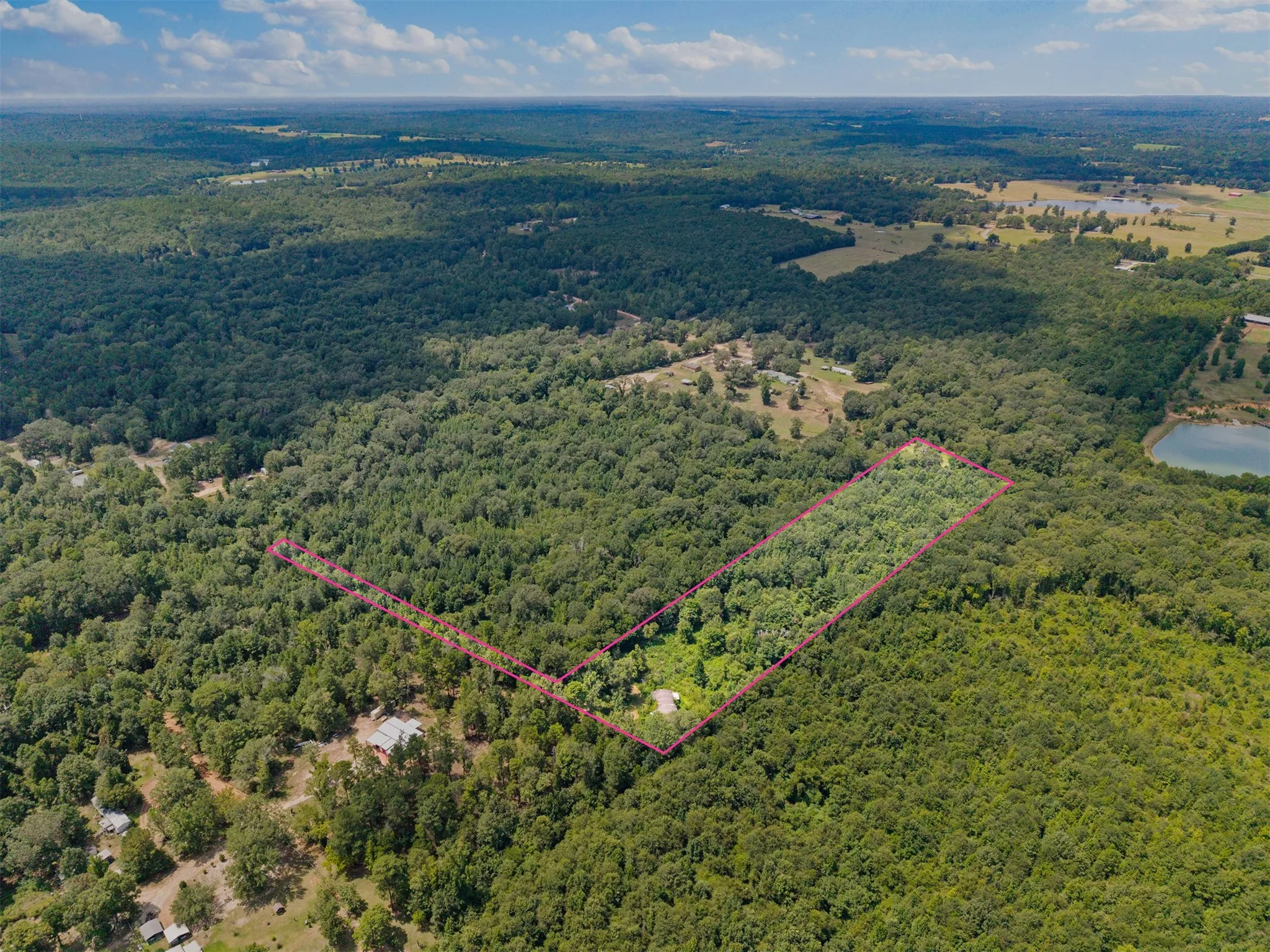Expansive wooded acreage with a delineated boundary, featuring a small structure and dense tree cover