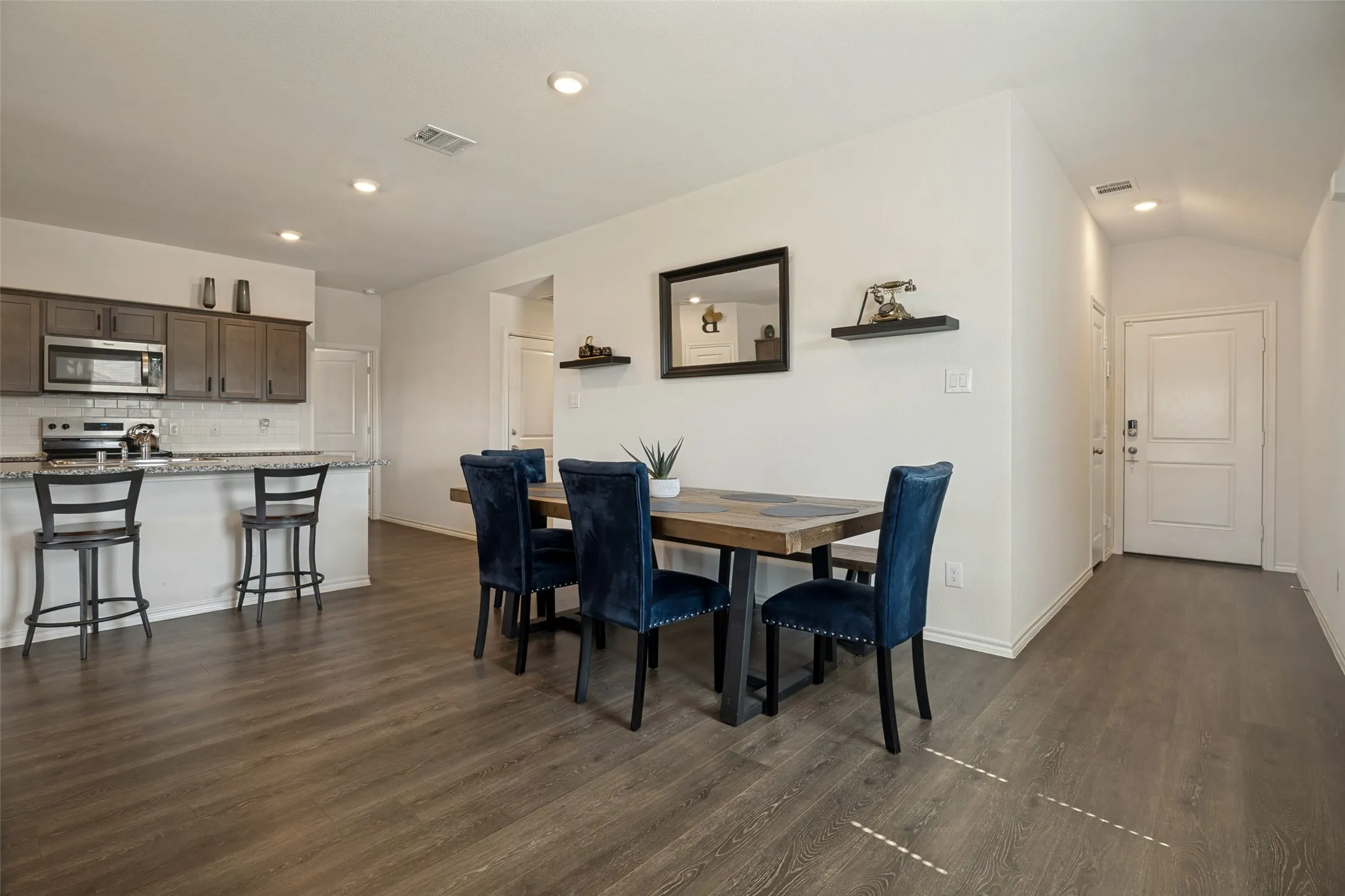 Kitchen featuring wood-finish cabinetry, stainless steel appliances, white subway tile backsplash, and a granite-style countertop with breakfast bar seating