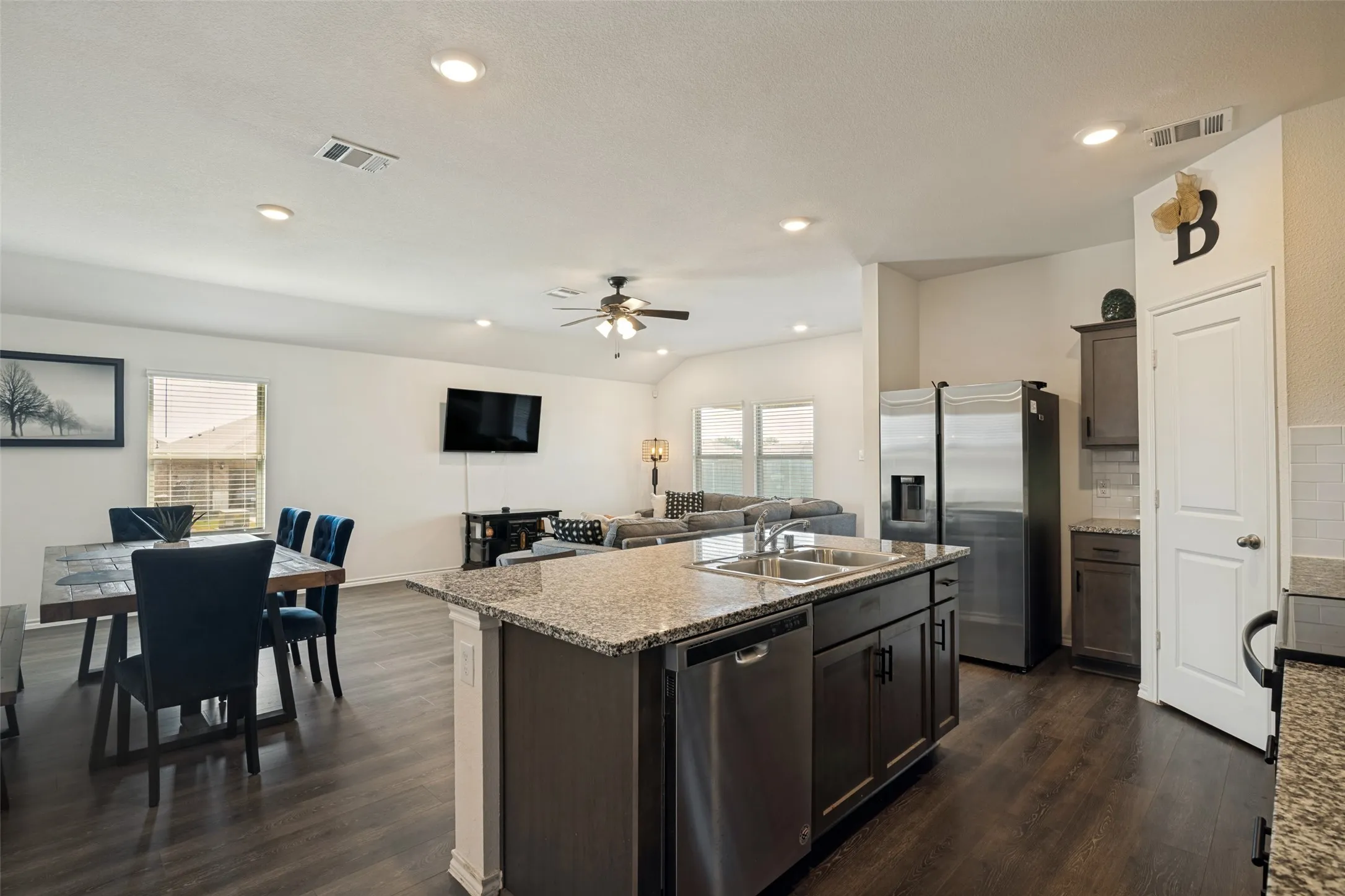 Open-concept layout featuring wood-finish flooring, recessed lighting, a ceiling fan, a kitchen island with a granite countertop, and stainless steel appliances