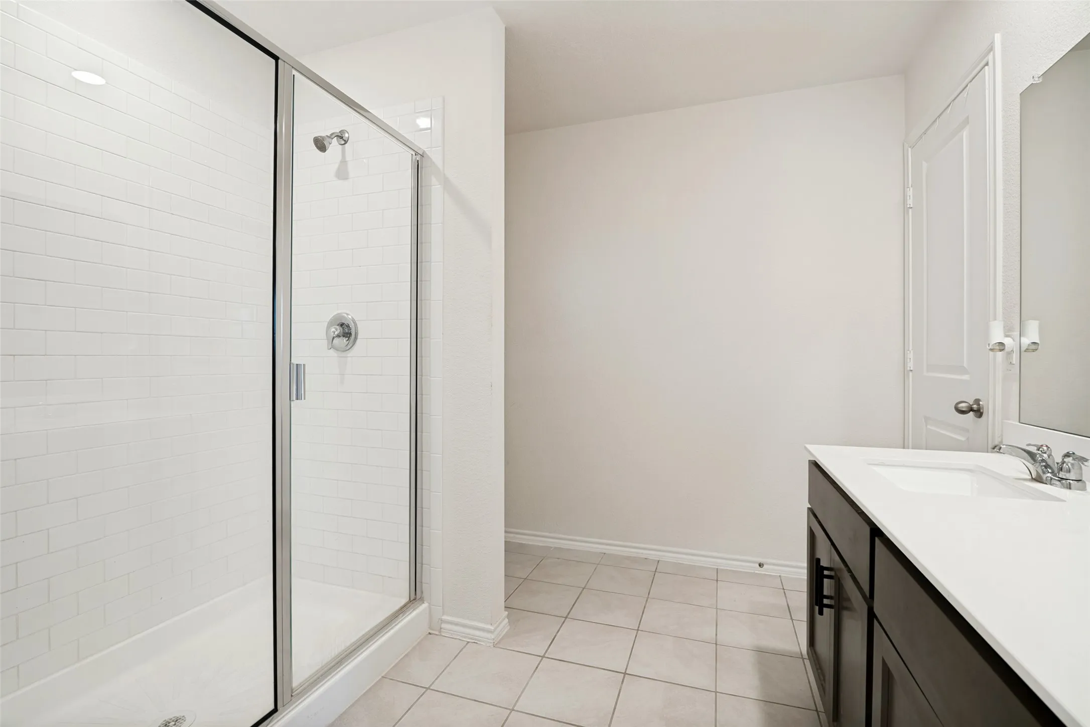 Glass-enclosed shower with subway tile surround, single vanity with cabinetry, white countertop, and tile flooring