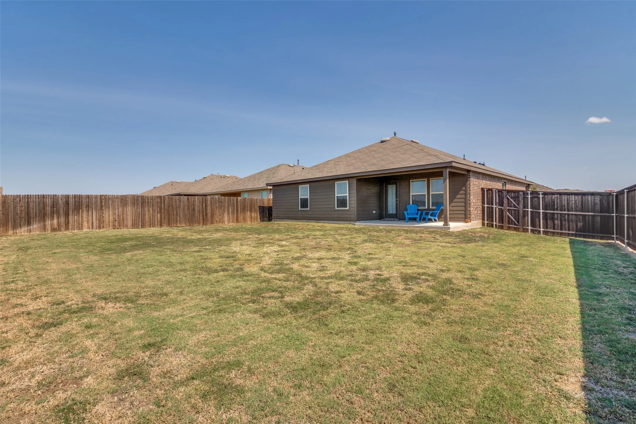 Expansive backyard featuring a full perimeter wooden fence, covered concrete patio, and exterior brick and siding finishes