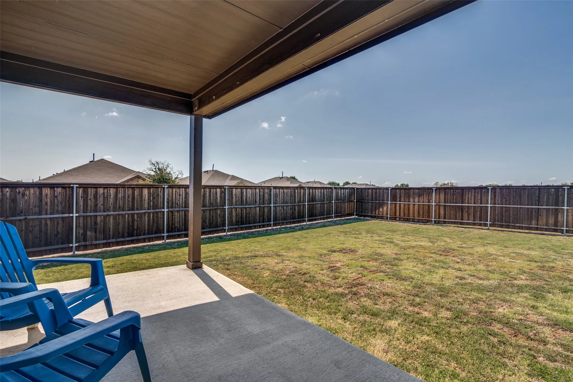 Covered patio with a concrete surface, leading to an enclosed backyard featuring a wood fence and a grass lawn