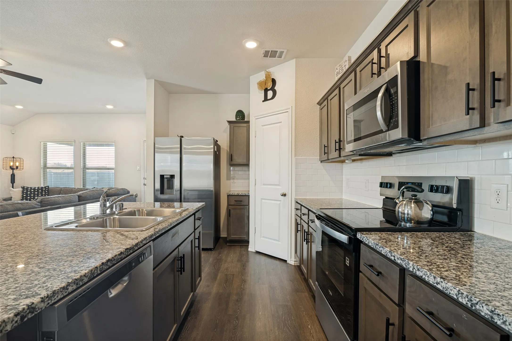 Kitchen featuring stainless steel appliances, wood-finish cabinetry, granite countertops, an undermount double-basin sink, and white subway tile backsplash