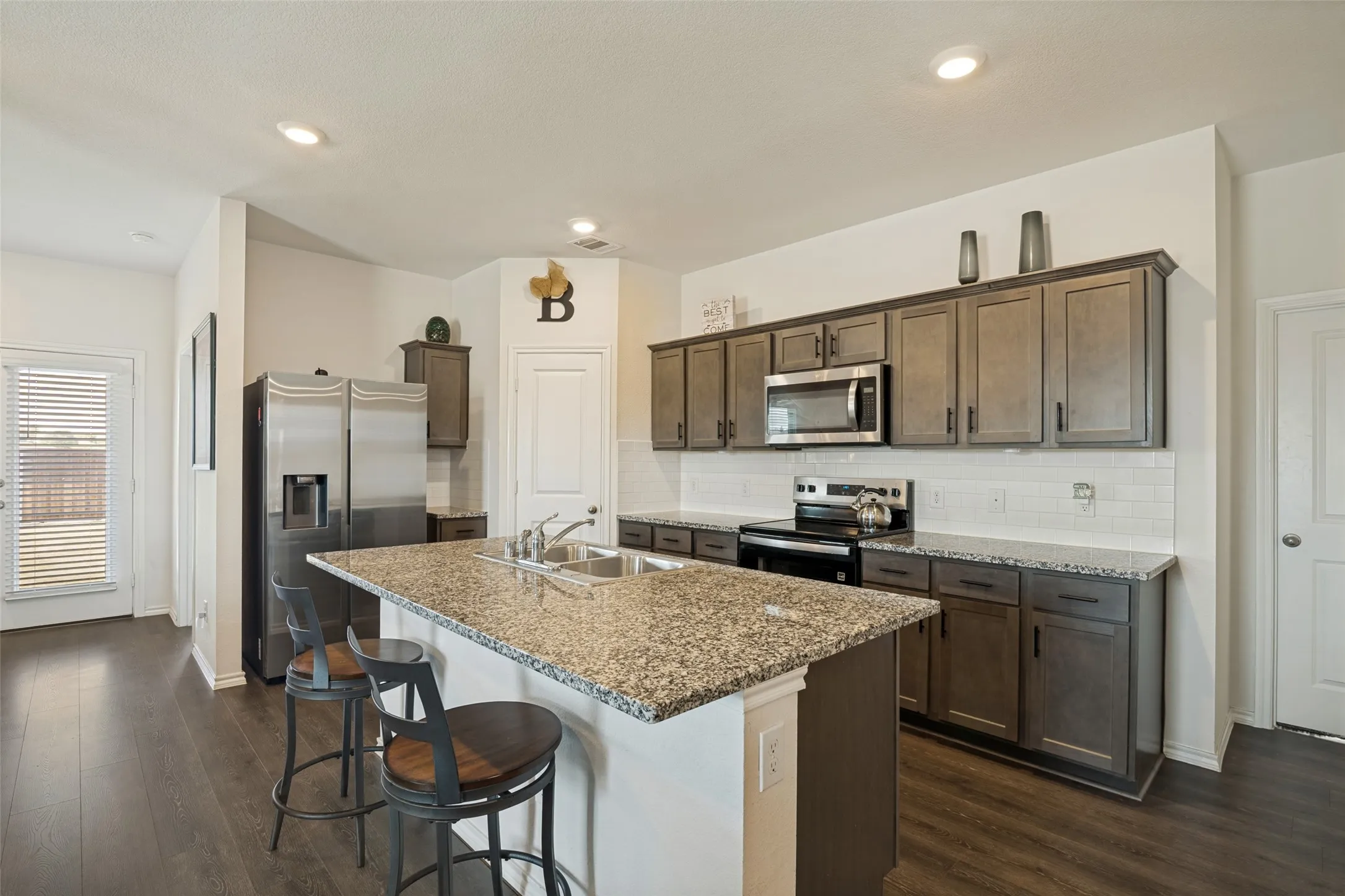 Kitchen featuring an island with granite countertops, stainless steel appliances, a white subway tile backsplash, wood-finish flooring, and recessed lighting