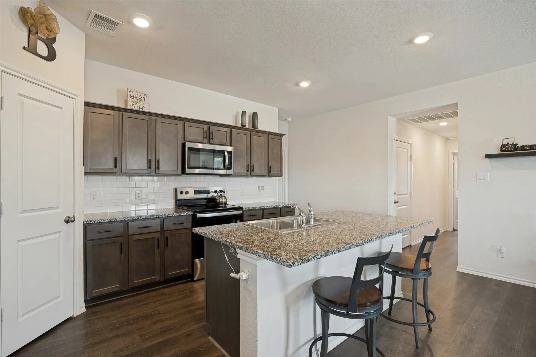 Spacious kitchen featuring wood-finish cabinetry, a white subway tile backsplash, stainless steel appliances, a large island with an undermount sink, and wood-finish flooring