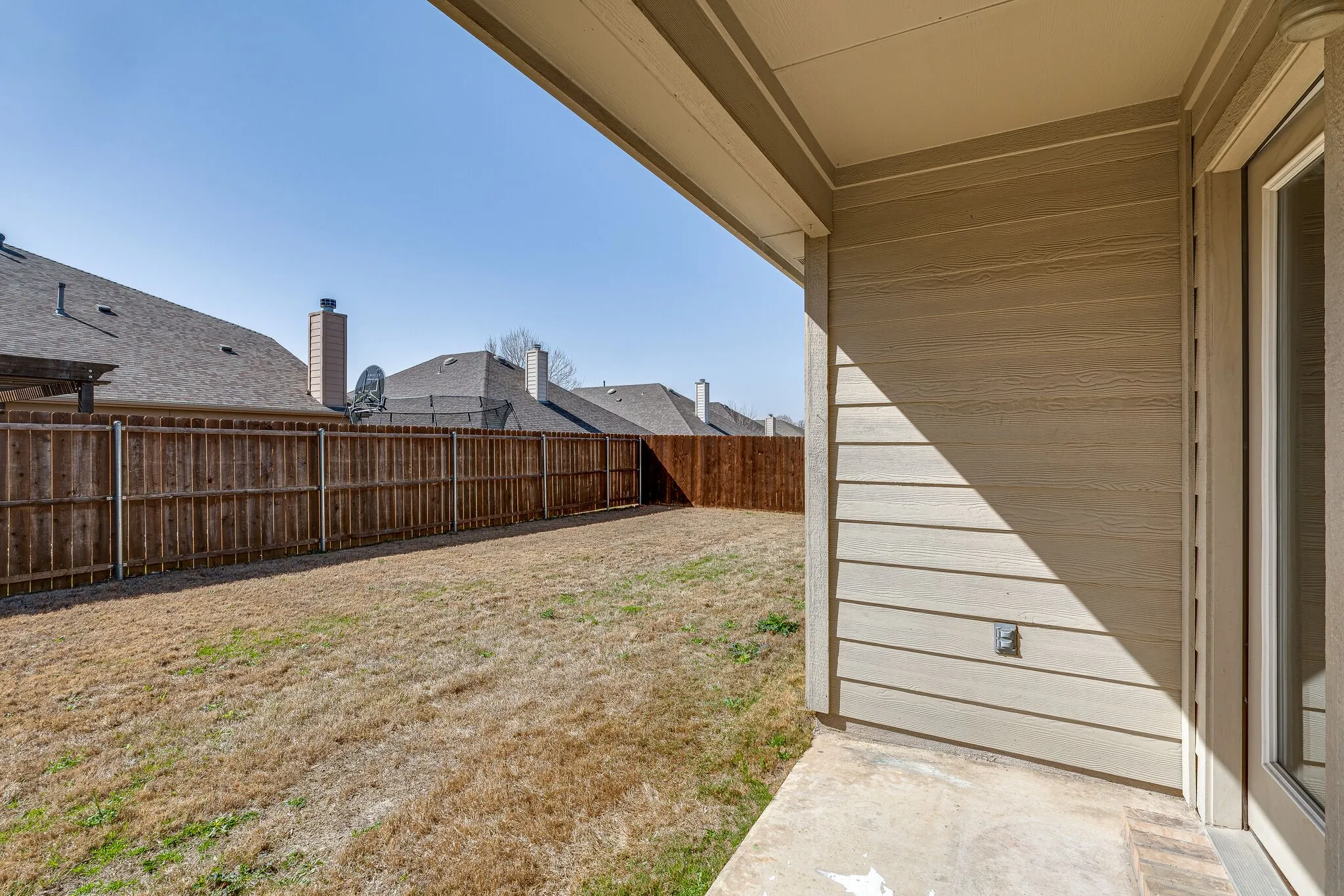 Expansive backyard with a full privacy fence, covered patio, and concrete patio surface