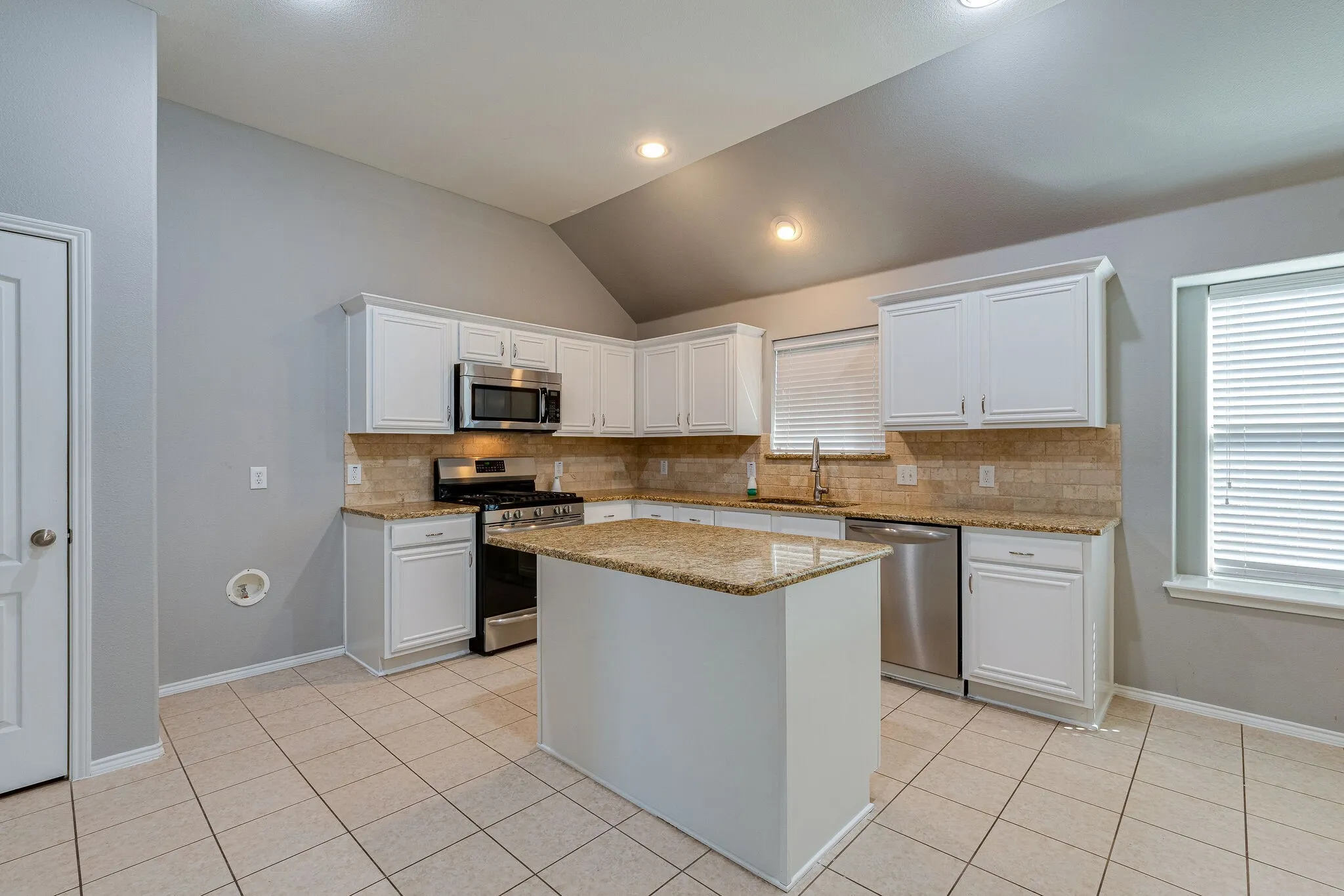 Kitchen featuring a vaulted ceiling, recessed lighting, white cabinetry, granite countertops, and stainless steel appliances