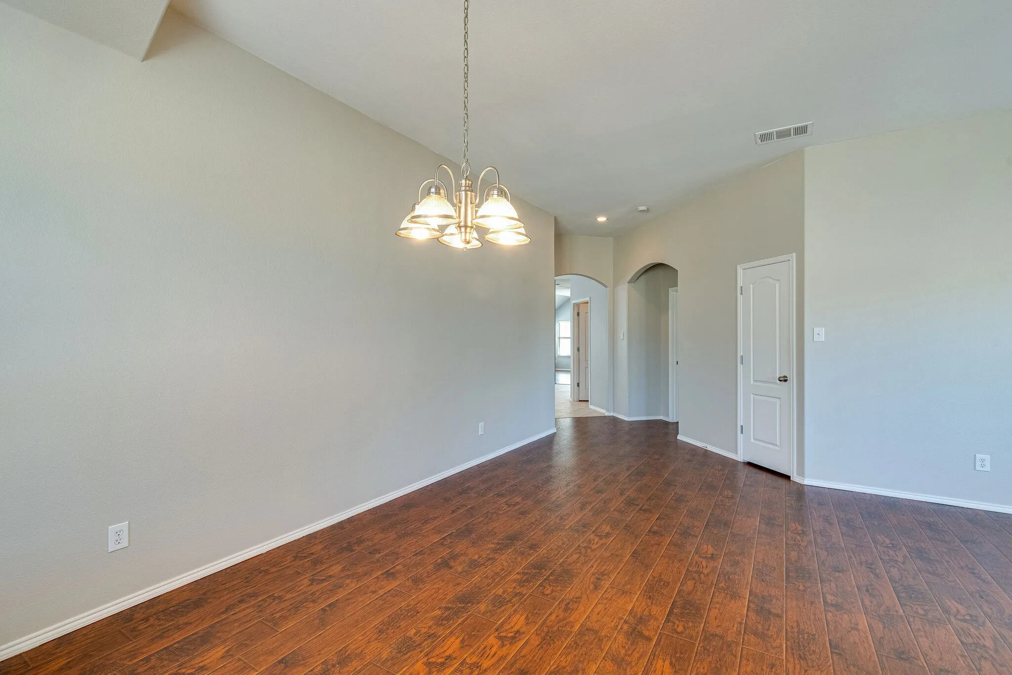 Vaulted ceilings with a chandelier, wood-finish flooring, light neutral wall tones, and arched doorways