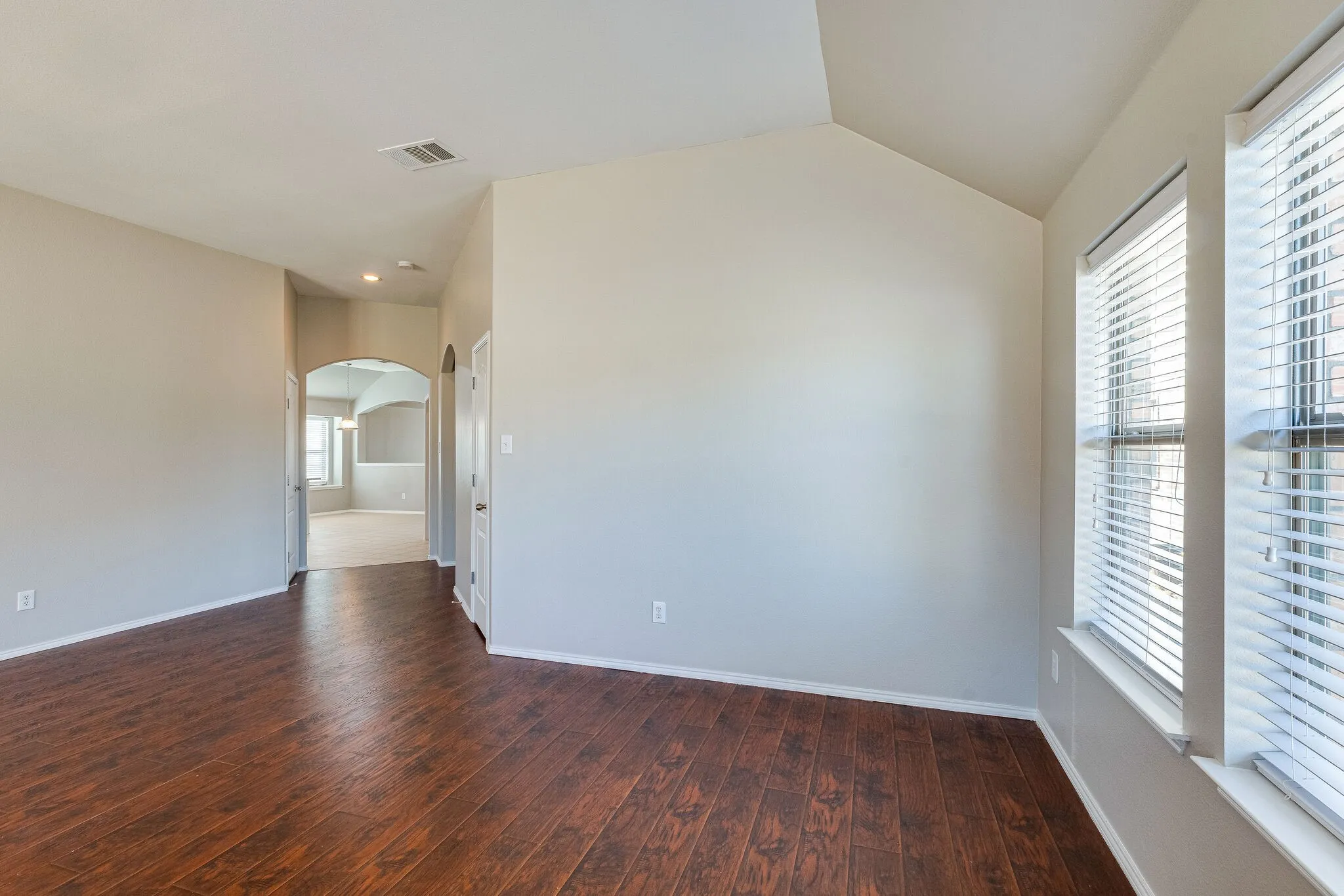 Wood-finish flooring throughout, vaulted ceiling, dual windows with blinds, arched doorways, and light neutral wall colors