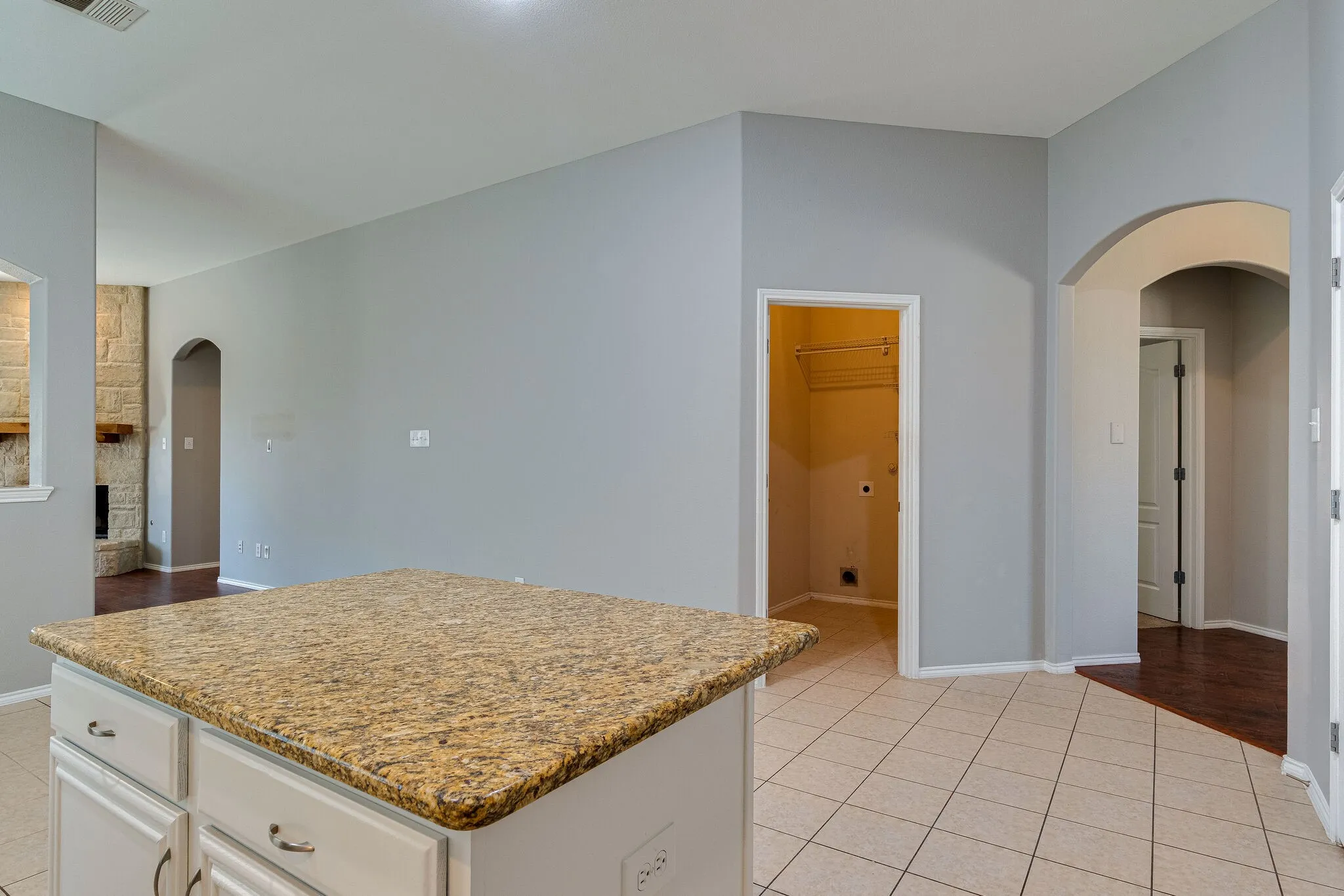 Kitchen island with a speckled countertop, white cabinetry with dark hardware, tile flooring, and arched doorways