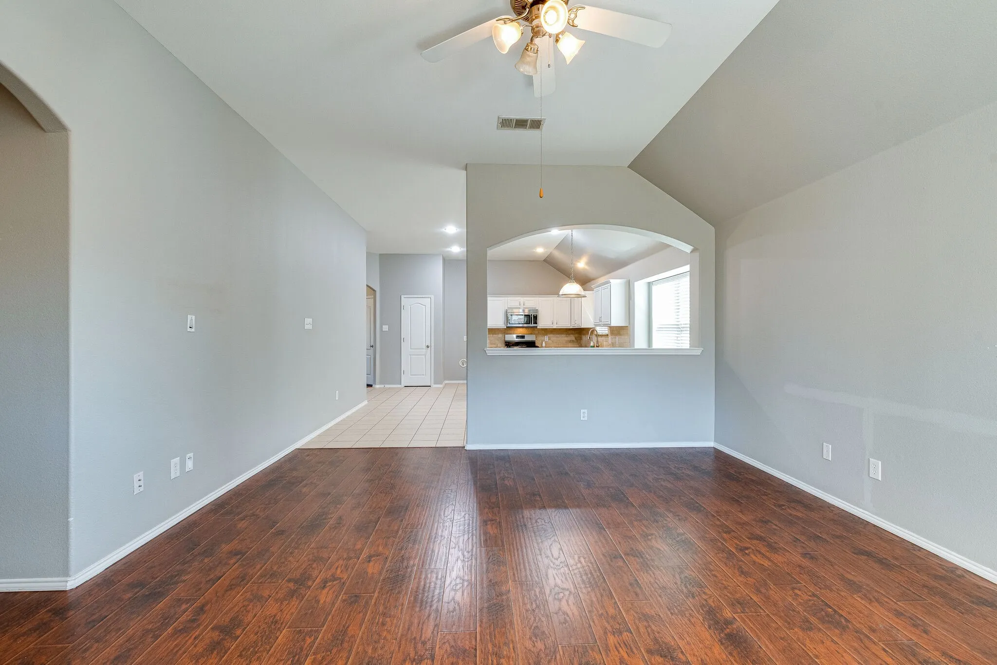 Wood-finish flooring, recessed lighting, ceiling fan, and arched pass-through window to kitchen