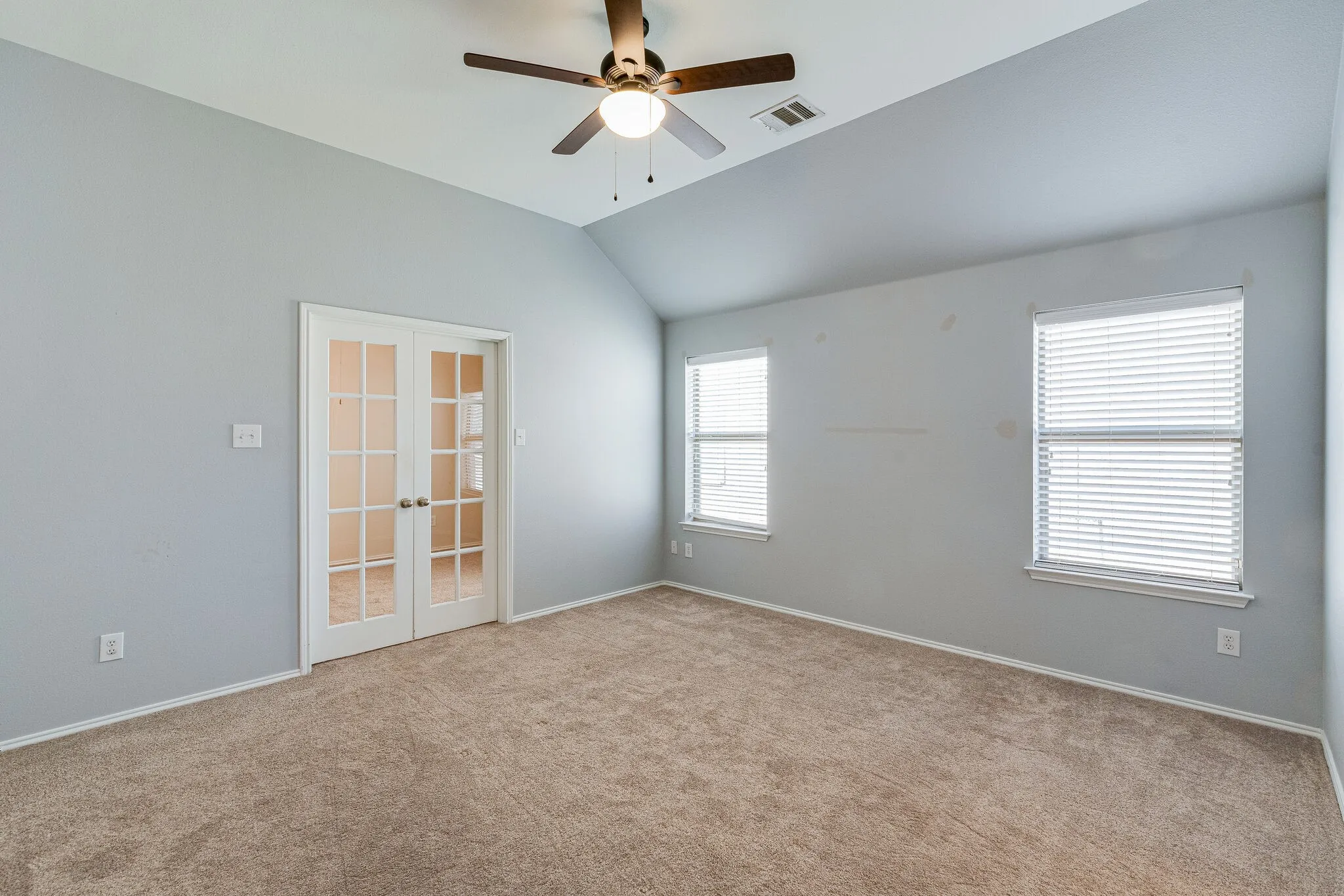 Vaulted ceiling with a ceiling fan, two windows with blinds, and double French doors, all complemented by wall-to-wall carpeting