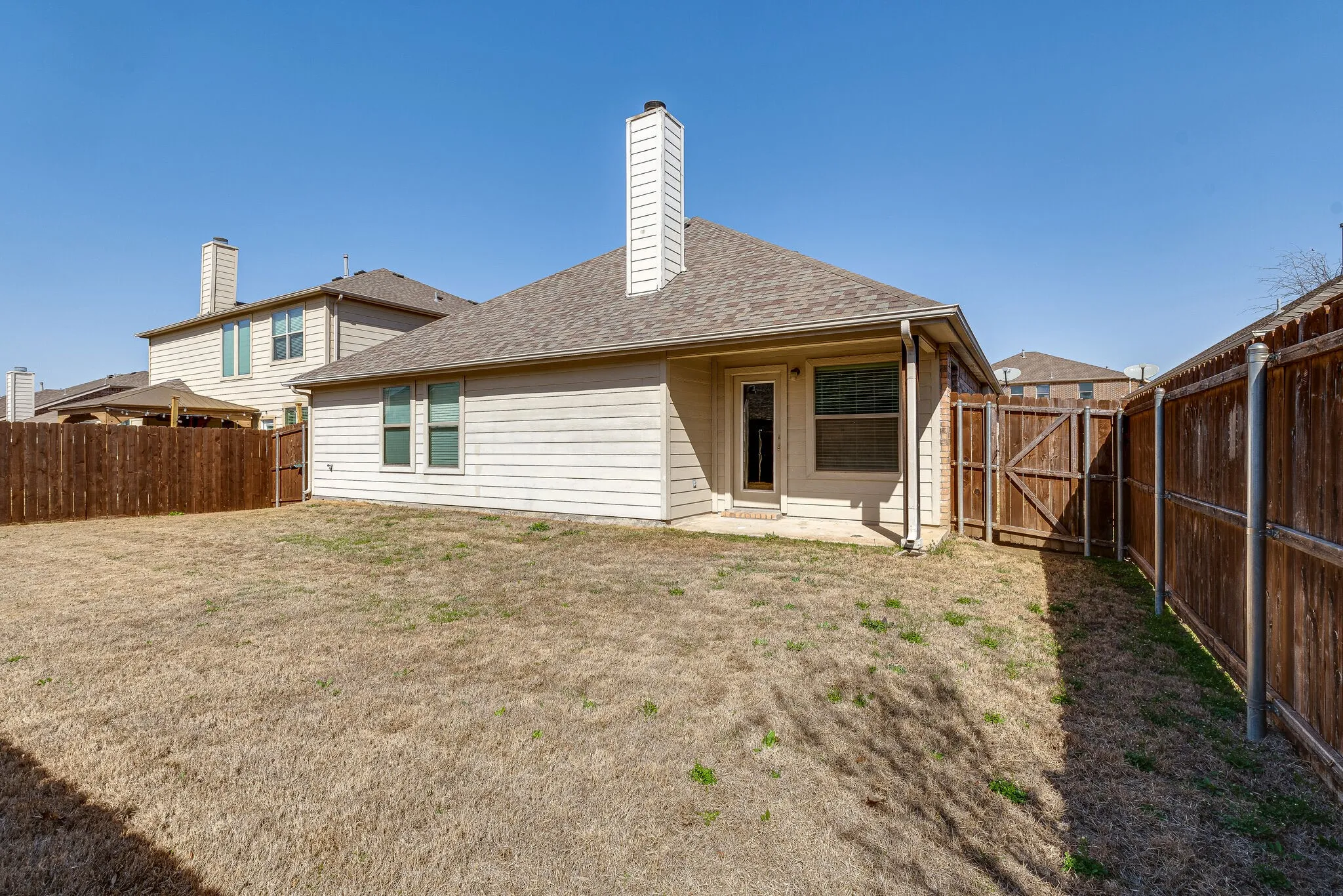 Exterior featuring light-colored siding, a shingled roof, a chimney, and a wooden privacy fence