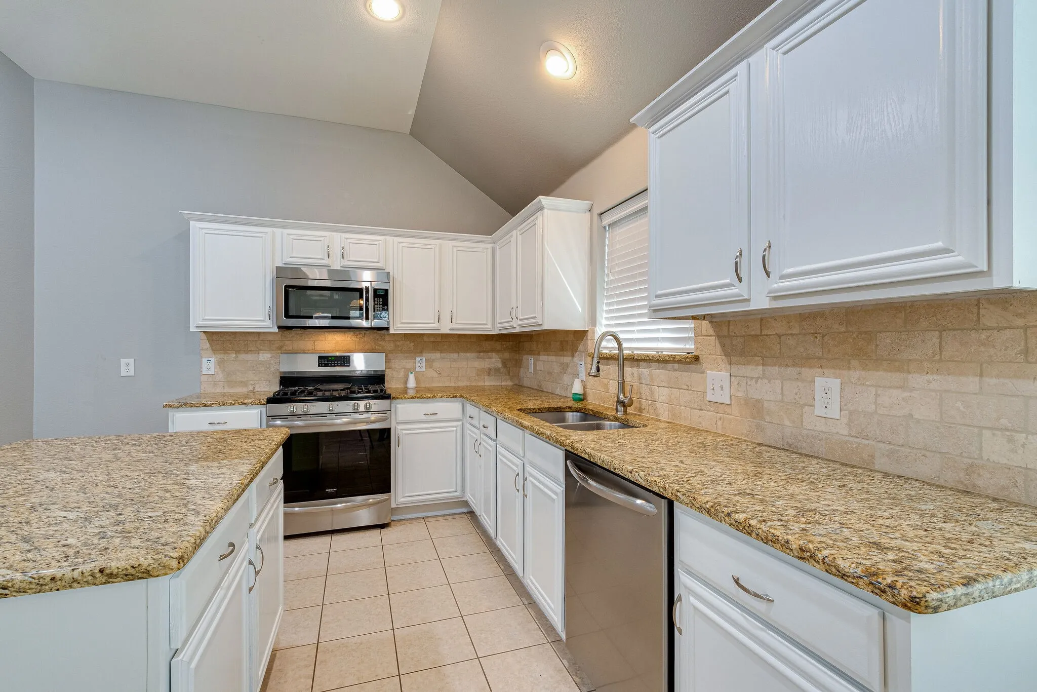 Kitchen featuring white cabinetry, stainless steel appliances, granite countertops, tile backsplash, and tile flooring