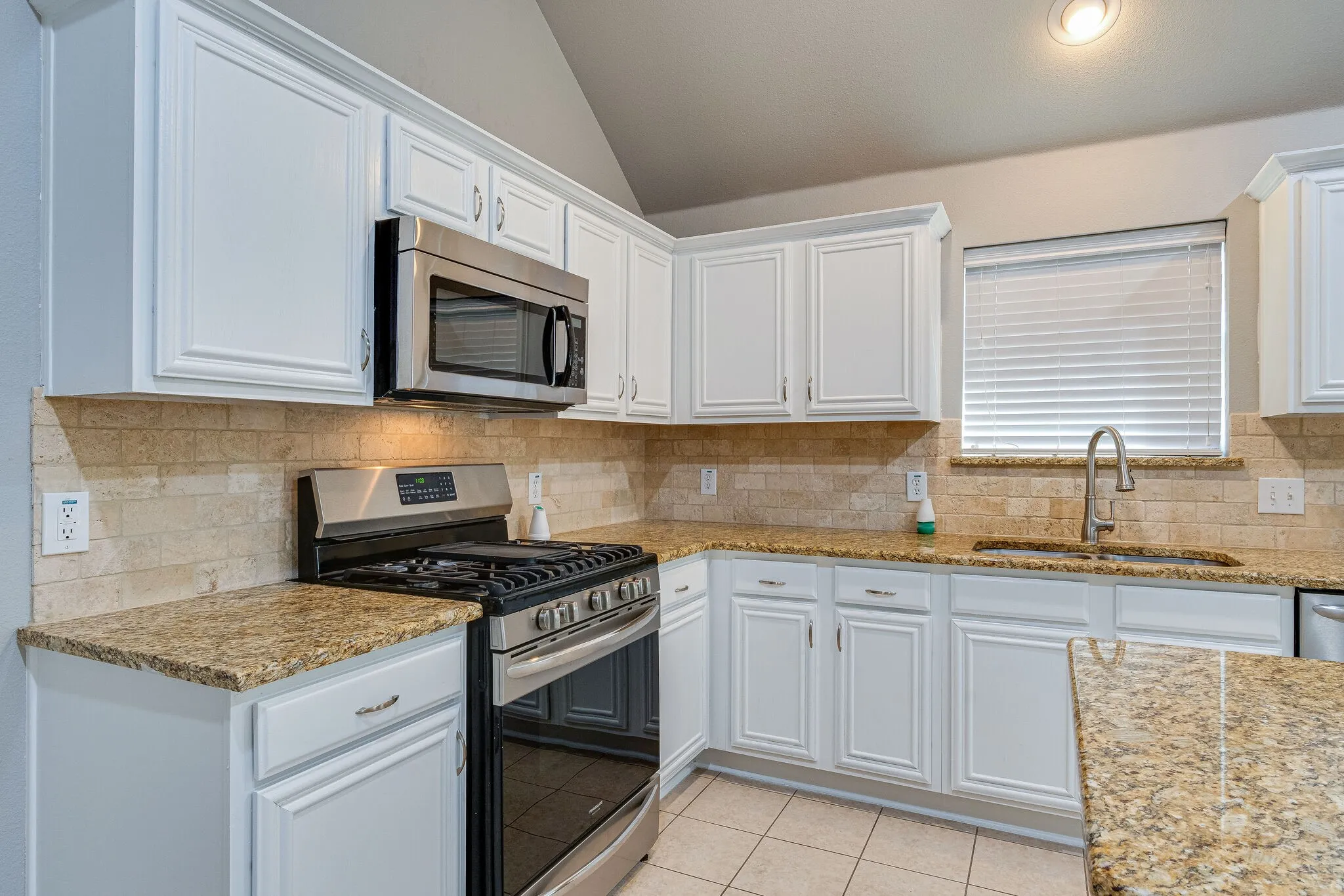 White cabinetry, stone countertops, stainless steel appliances, tile backsplash, and recessed lighting