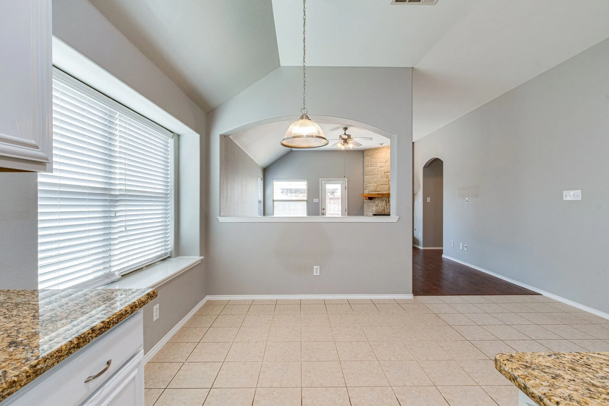 Kitchenette featuring tile flooring, granite-style countertops, white cabinetry, a window with horizontal blinds, and a built-in archway
