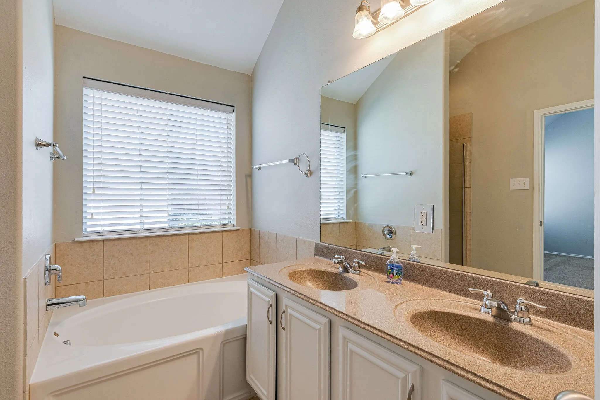 Dual vanity with integrated sinks, a large mirror, a built-in tub, and a window with blinds