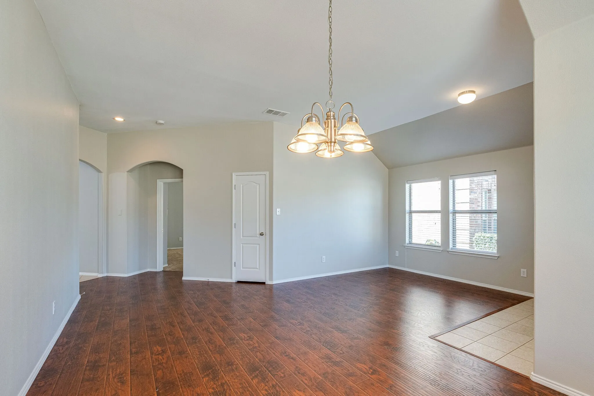 Spacious room featuring wood-finish flooring, vaulted ceiling, and a multi-light chandelier