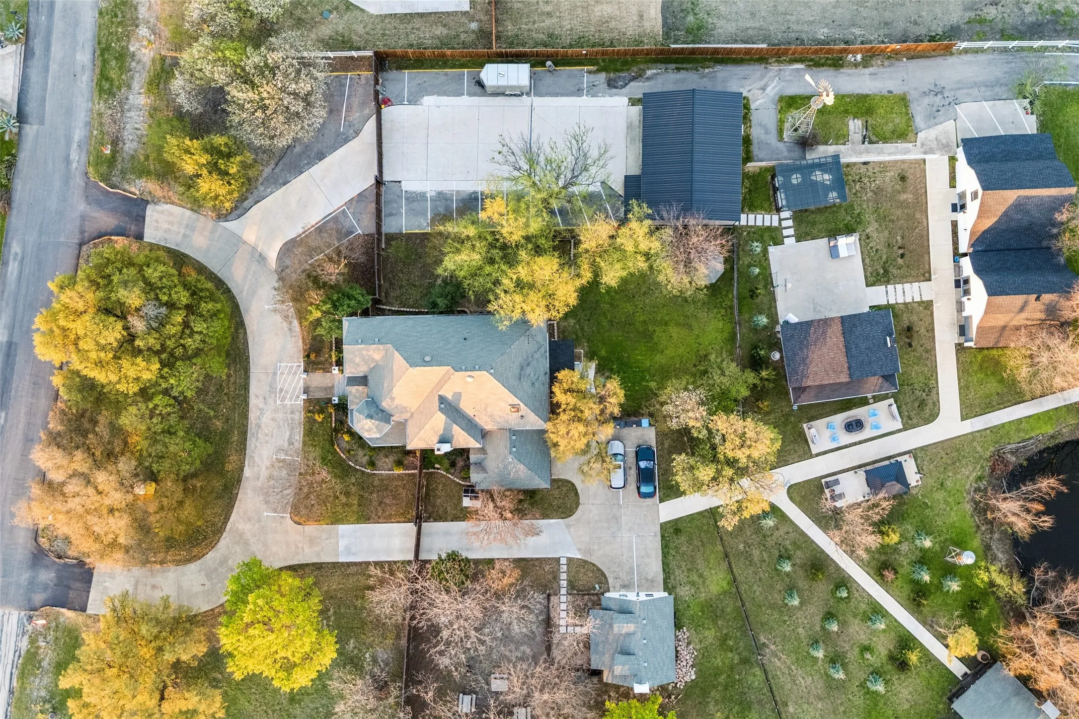 Expansive property with a curvilinear driveway, mature trees, and a detached building with a dark roof