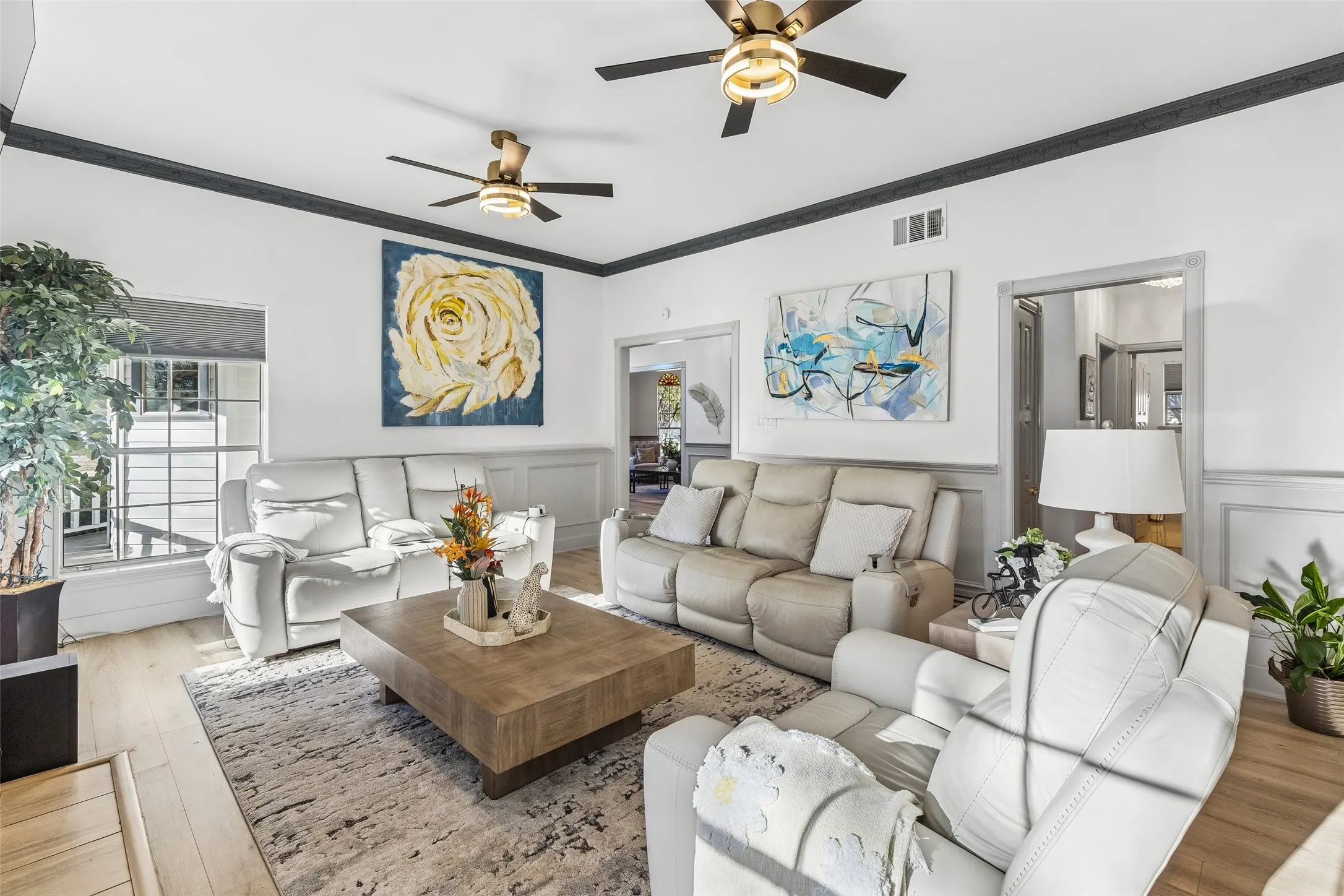 Spacious living area featuring wood-finish flooring, ceiling fans with integrated lighting, and crown molding