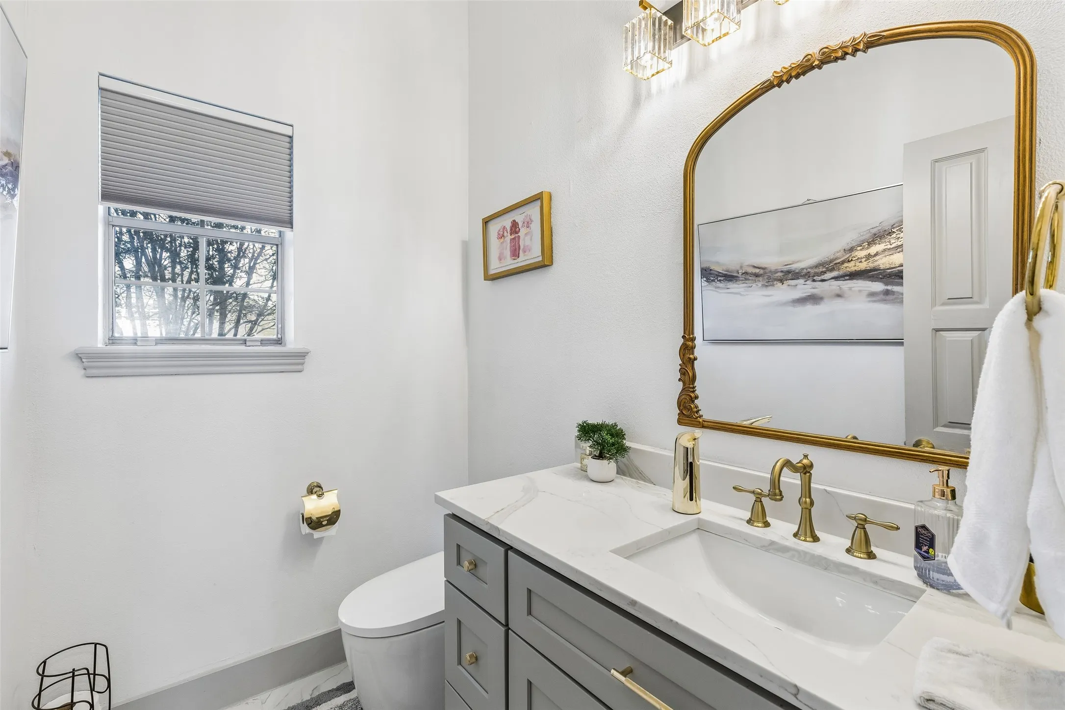 Vanity with a white countertop and integrated sink, brass fixtures, decorative framed mirror, and a modern light fixture