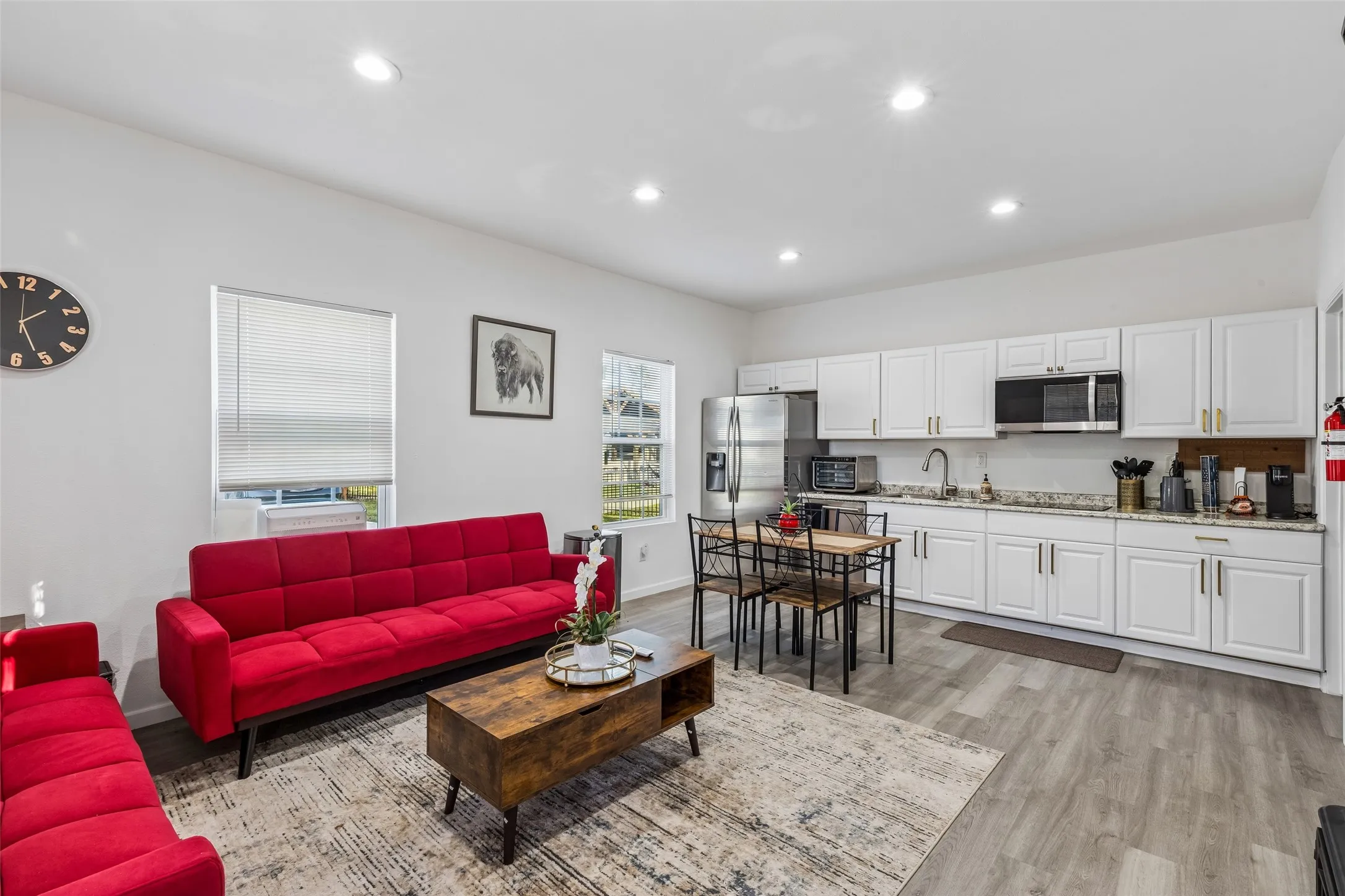 Open-concept living space featuring recessed lighting, light wood-finish flooring, white kitchen cabinetry with gold-tone hardware, and stainless steel appliances