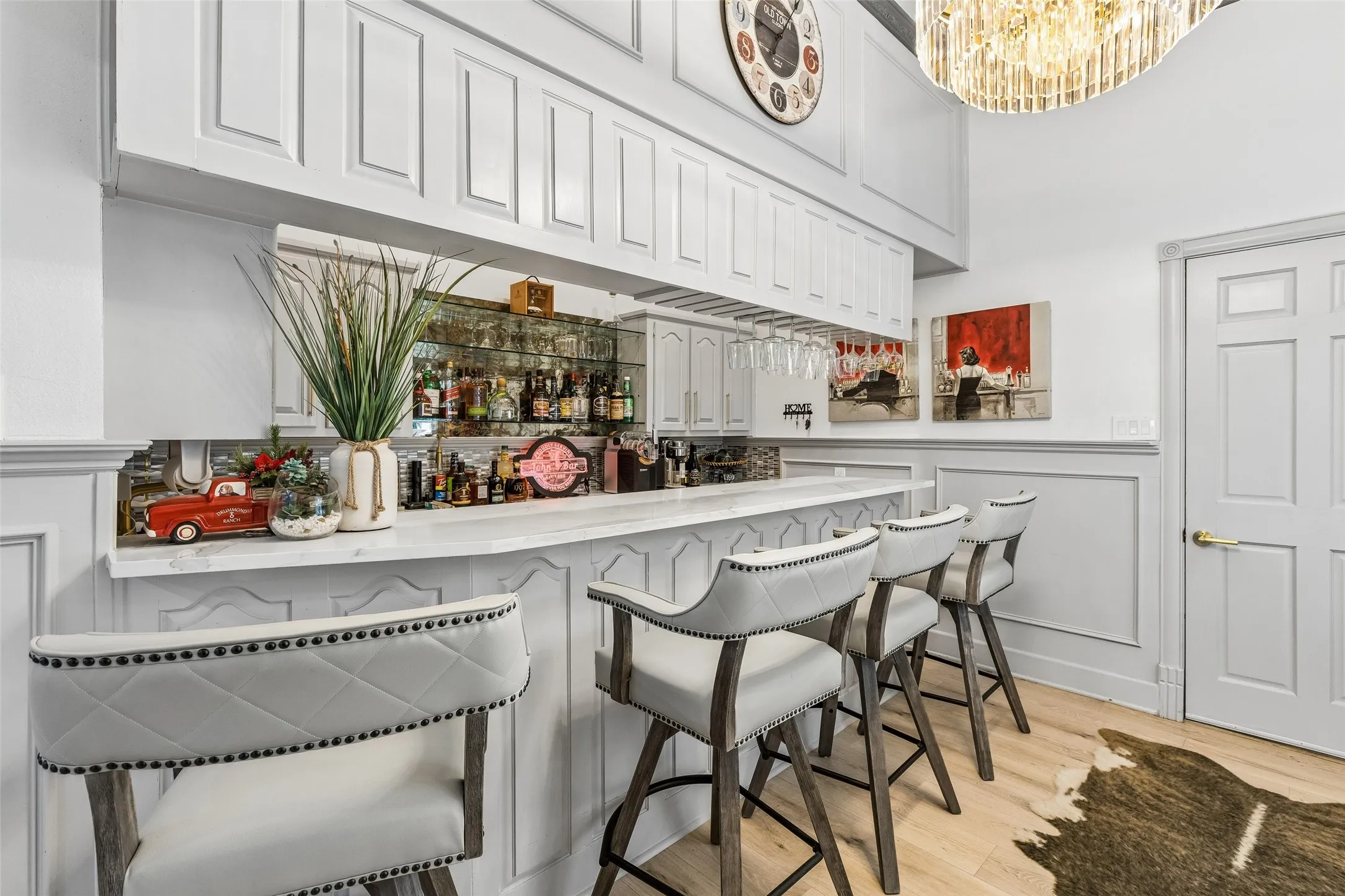 Built-in bar with a light-toned countertop, integrated glass racks, upper cabinetry, and paneling