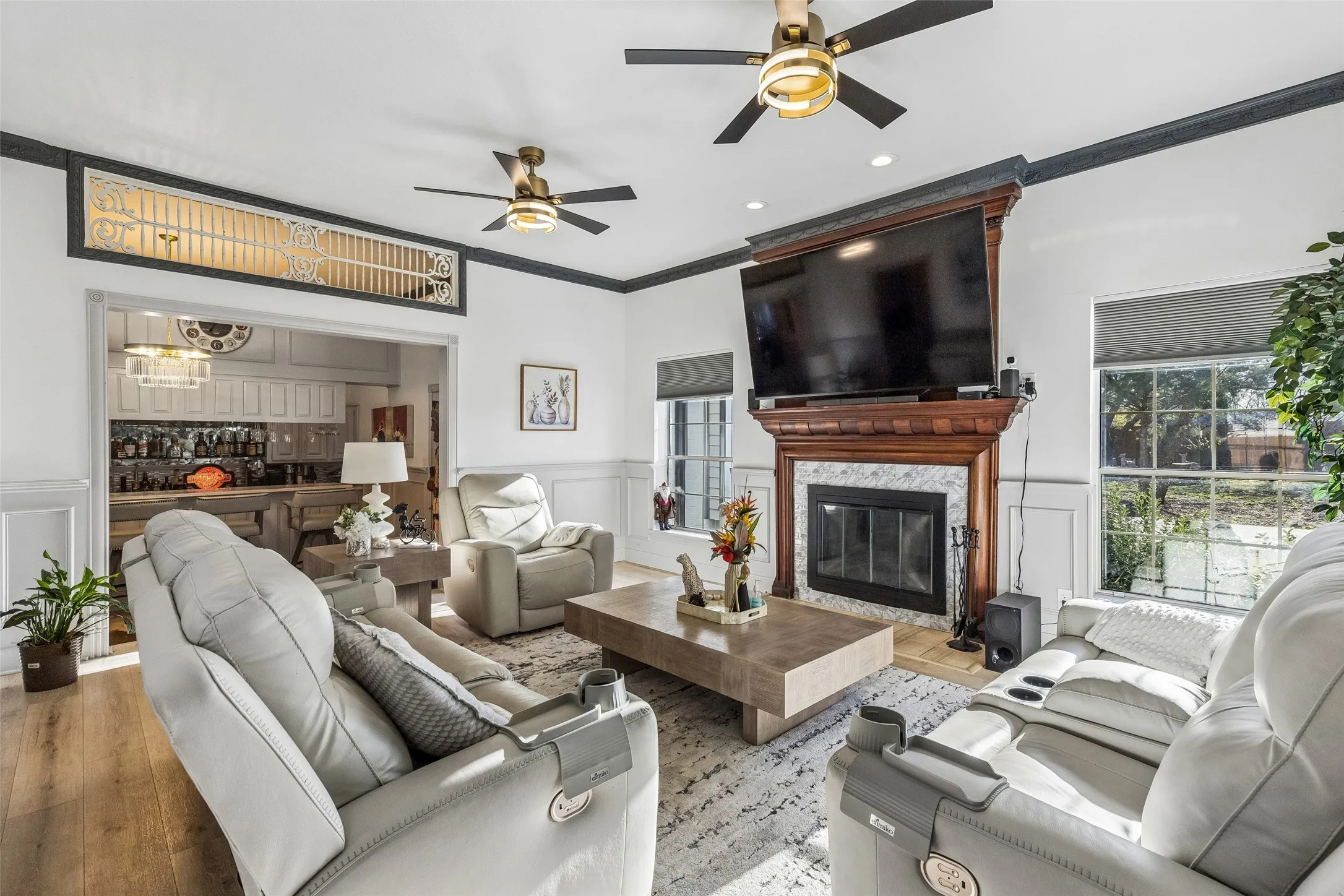 Living area with a wood-finish flooring, a fireplace featuring a wood mantel and stone surround, and multiple ceiling fans