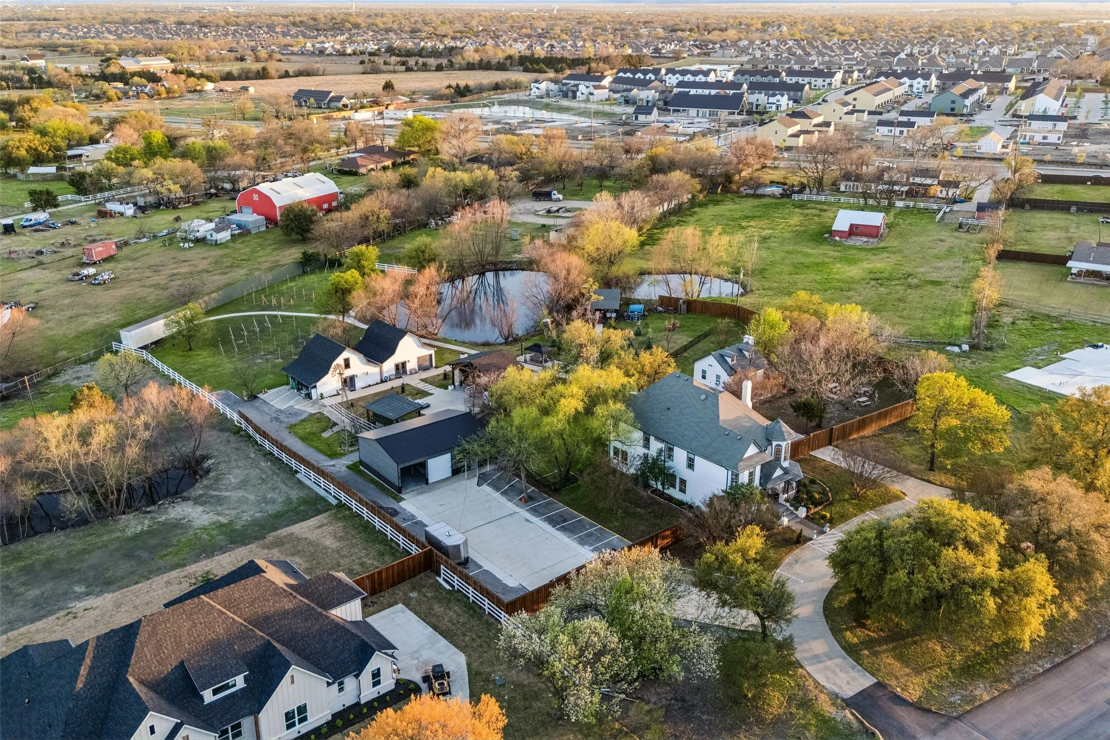 Expansive property featuring a pond, white picket fencing, and multiple outbuildings