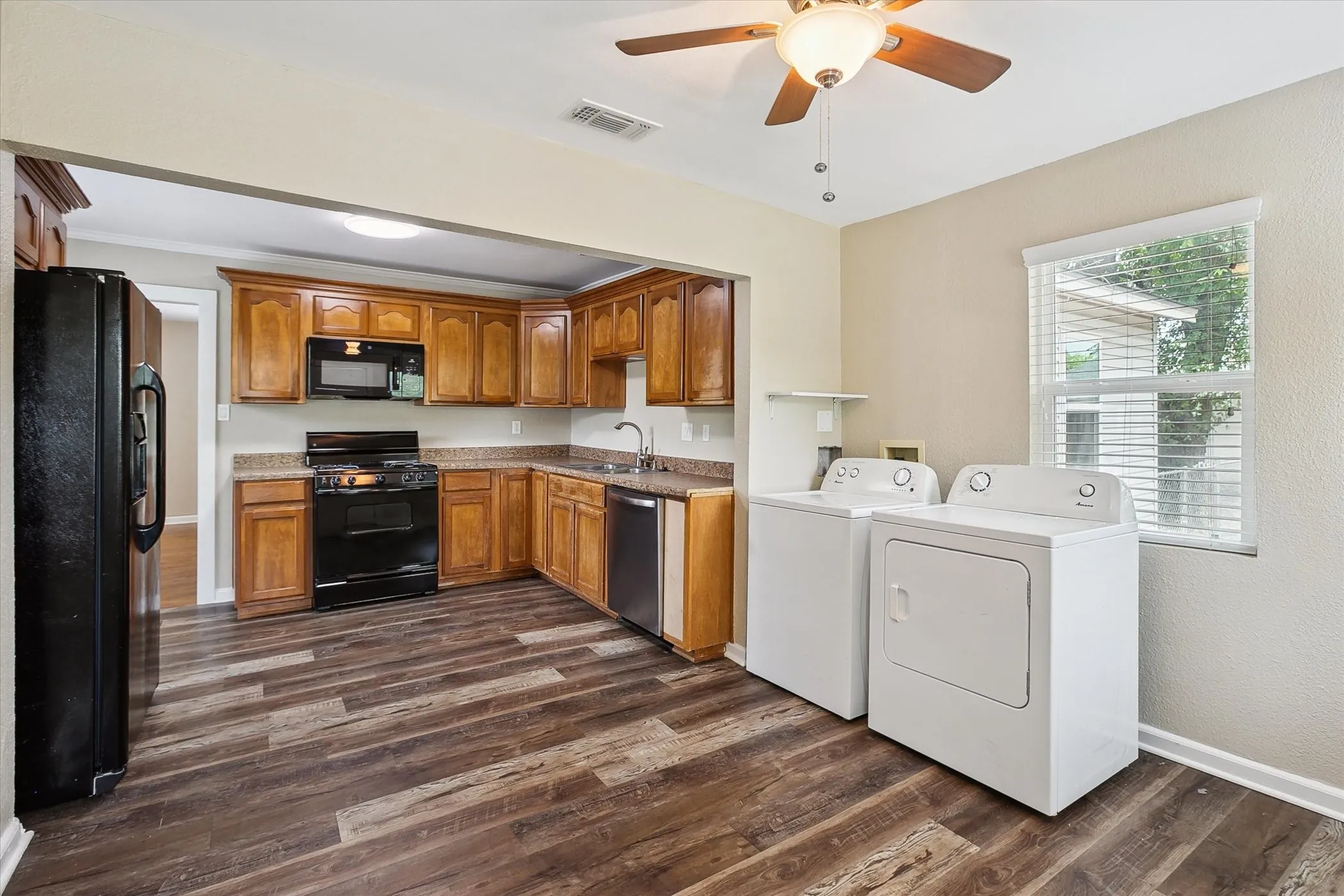 Kitchen featuring laminate flooring, wood cabinetry, built-in microwave, refrigerator, washer and dryer and a ceiling fan with integrated lighting